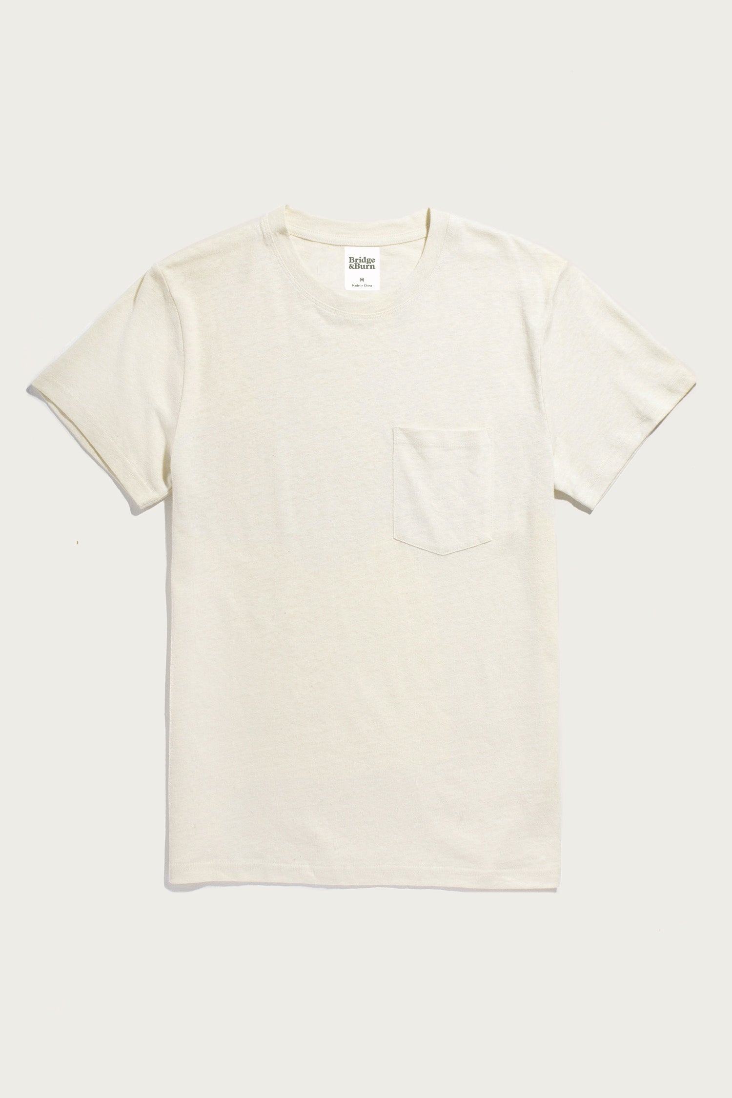 The Bridge & Burn Organic Hemp Pocket Tee in Ivory is a vintage-style, short-sleeve t-shirt with a round neckline and single chest pocket, shown laid flat on a light background.