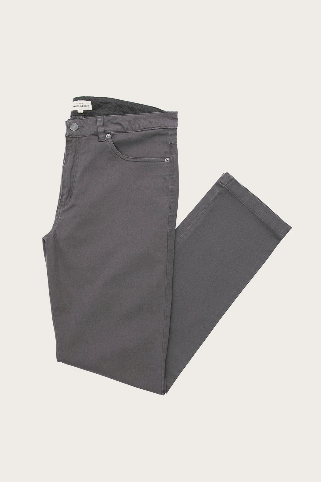The Bridge & Burn Polk Pant in Charcoal, neatly folded with one leg crossed over the other, is displayed on a plain white background.
