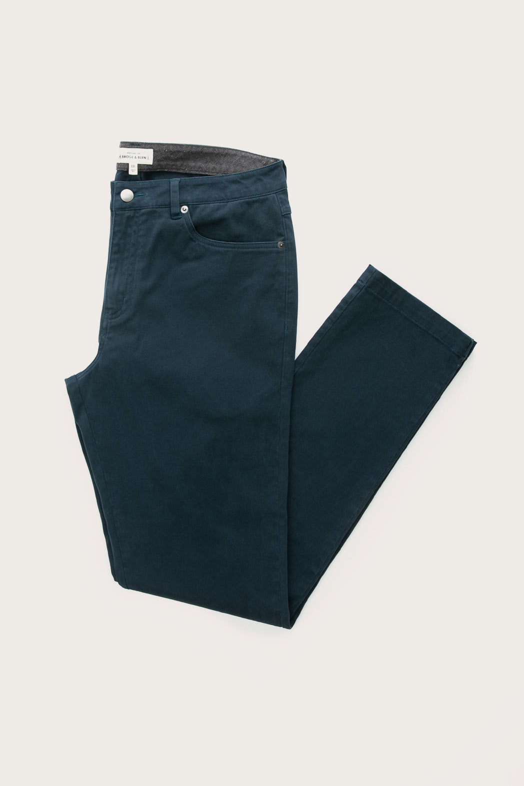 The Bridge & Burn Polk Pant in navy—a pair of straight-fit pants with front pockets and a visible waistband lining—neatly folded and displayed on a plain white background.
