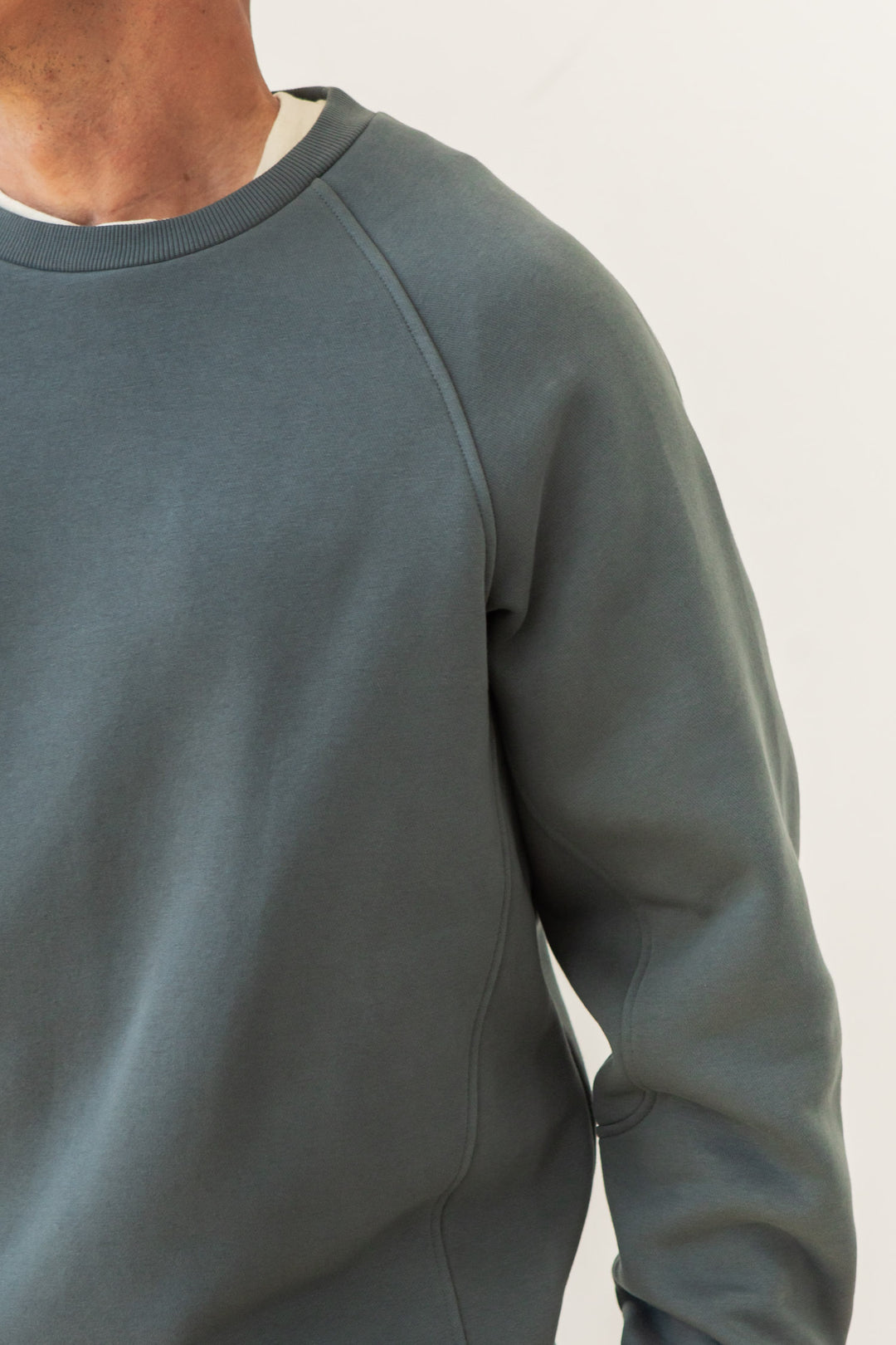 A person wears the Bridge & Burn Lincoln Crew Sweatshirt in Slate, shown from shoulders to waist against a plain light background. Only part of the face and neck are visible.