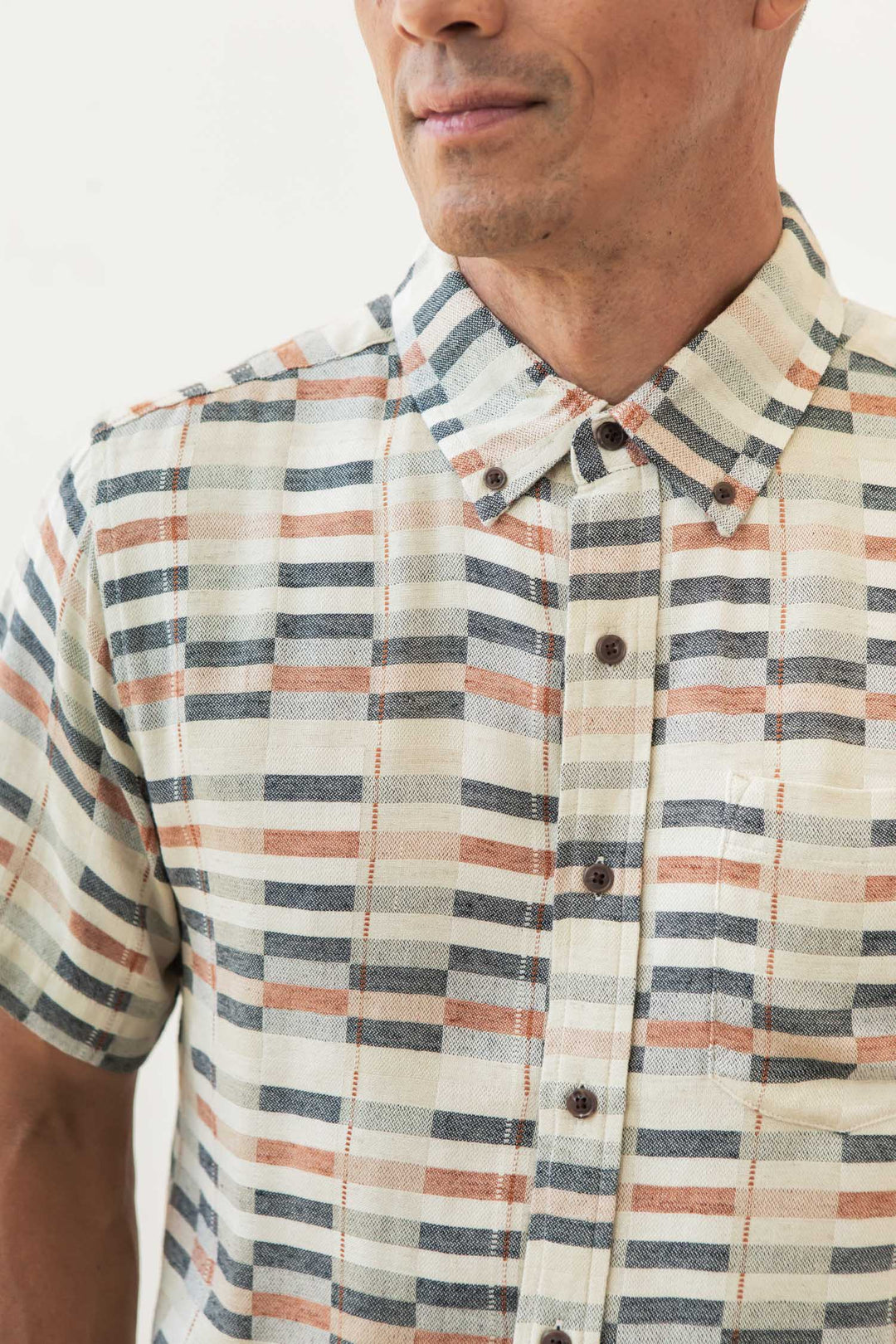 A man wears the Bridge & Burn Jordan Slim Shirt in Broadway Stripe—a modern, short-sleeve, button-up with a striped pattern. The image captures his upper torso and part of his face against a light background.