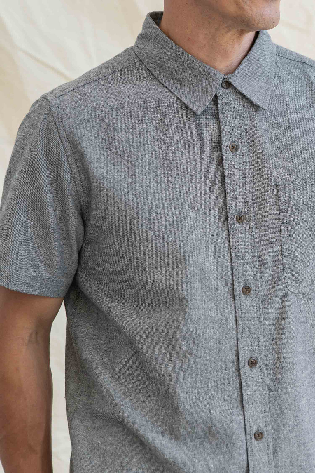 A person wearing the Bridge & Burn Malcolm Shirt in Iron Chambray stands against a light background, showing their upper torso and part of their face.