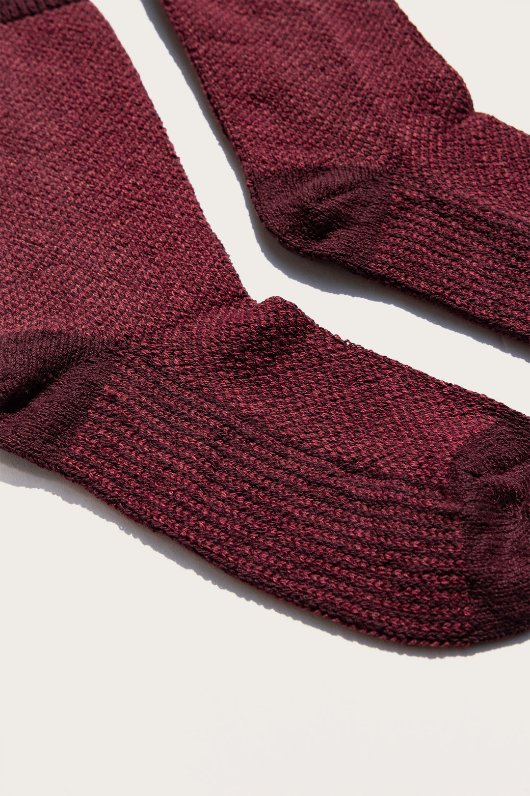 A close-up of the Bridge & Burn Helix Sock in Burgundy, featuring textured eco-friendly knit, laid flat on a light background.