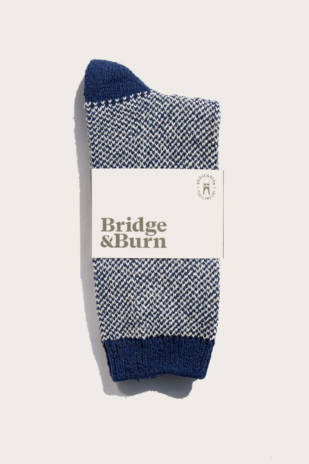 A pair of Bridge & Burn Helix Sock / Navy, featuring a blue and white pattern, recycled material, branded label, and round logo, displayed on a plain white background.