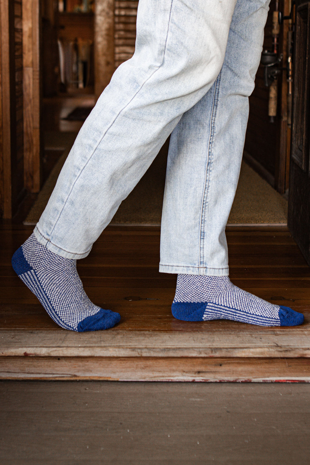 Wearing Bridge & Burn’s Helix Sock in Navy and light blue jeans, a person steps from a wooden floor onto the porch.