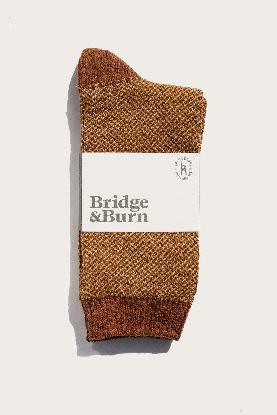 A pair of Helix Sock / Ochre by Bridge & Burn, textured brown and neatly folded with a white label featuring the brand name in bold letters, displayed against a plain white background.