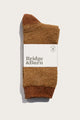A pair of Helix Sock / Ochre by Bridge & Burn, textured brown and neatly folded with a white label featuring the brand name in bold letters, displayed against a plain white background.