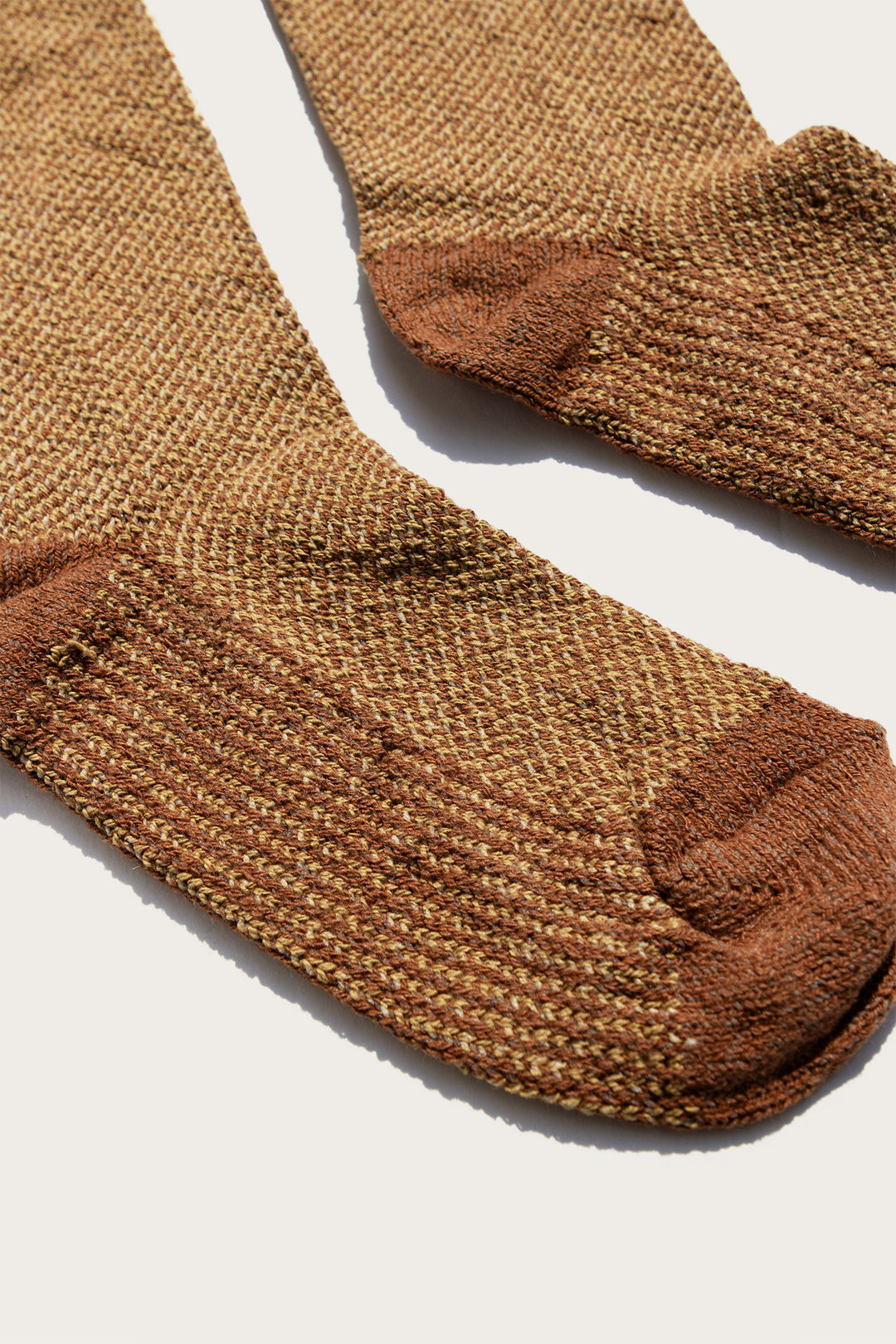 A close-up of the Bridge & Burn Helix Sock in Ochre, featuring textured brown and tan fabric with darker brown heel, toe, and cuff, laid flat on a light surface.