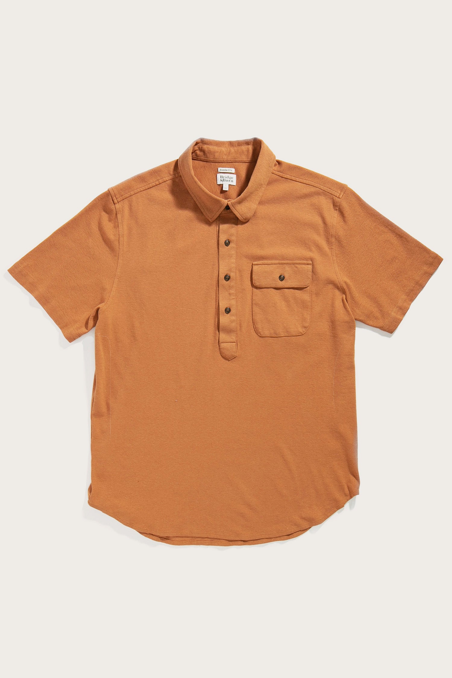 The Bridge & Burn Gary Knit Pullover in Clay Red Jersey is a men's casual short-sleeve polo with a collar, three-button placket, and buttoned chest pocket, crafted from soft jersey knit and shown laid flat on a white background.