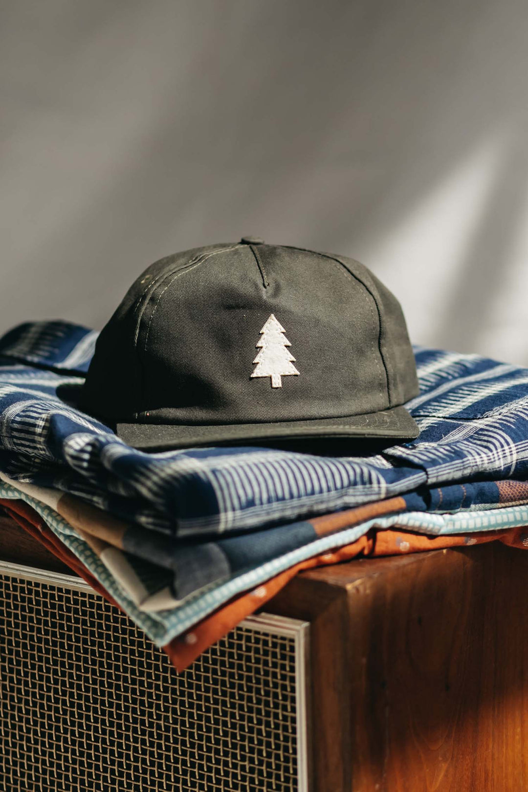 The Bridge & Burn Tree Cap / Olivewood sits atop folded patterned blankets on a wooden speaker, all softly illuminated by natural light.
