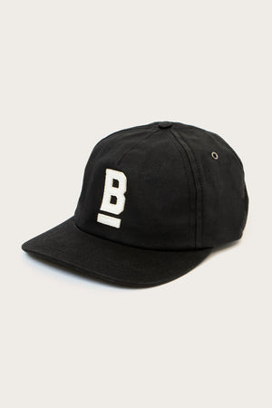 The B Flat Waxed Cap in black by Bridge & Burn features a white embroidered underlined letter B on the front, set against a plain light background.