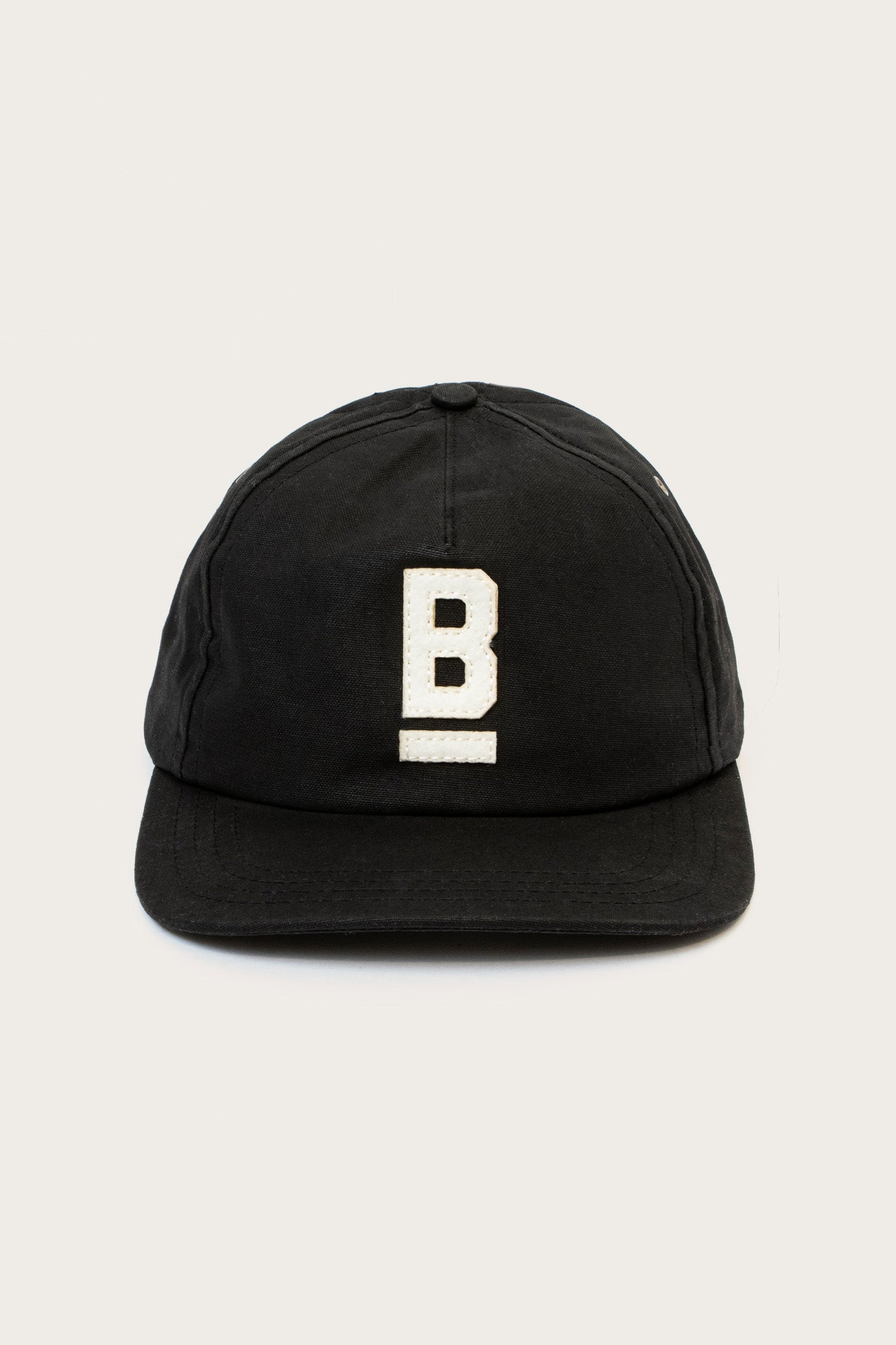 The B Flat Waxed Cap in black by Bridge & Burn features a white embroidered capital B with an underline on the front, set against a plain light background.