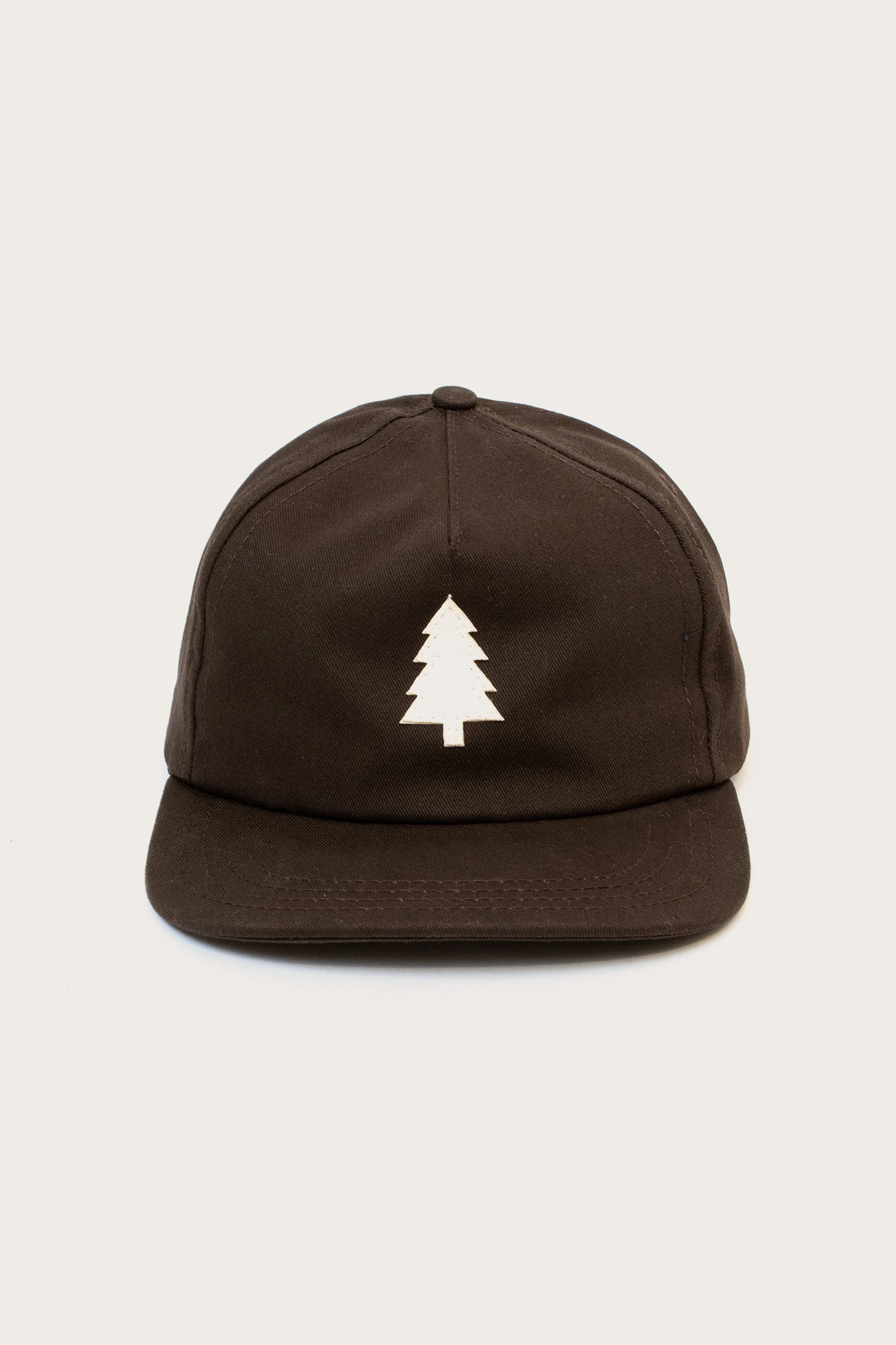 The Tree Cap / Espresso by Bridge & Burn is a black cotton twill hat with a minimalist white pine tree graphic on the front, shown against a plain light background.