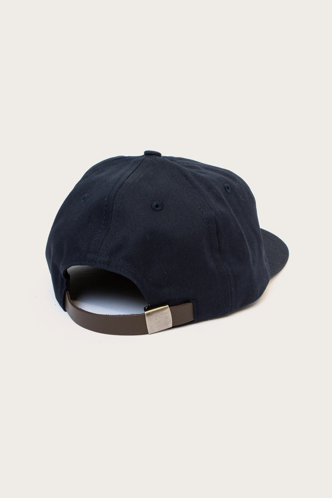 The Bridge & Burn Tree Cap / Navy is shown from the back, highlighting its brown leather adjustment strap with a silver buckle, set against a plain light background.