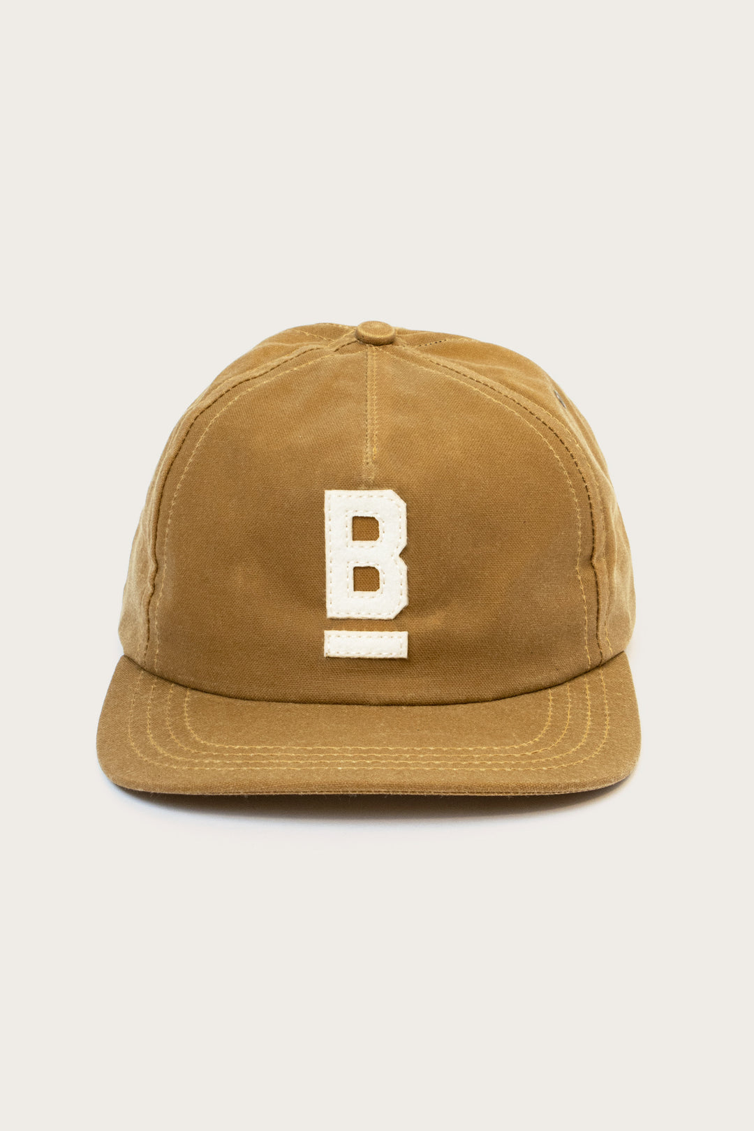 The Bridge & Burn B Flat Waxed Cap in brown features British Millerain waxed canvas, a flat brim, and a white embroidered underlined "B" on the front—ideal as your wet weather hat.