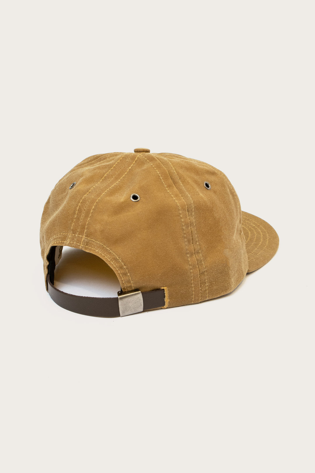 The Bridge & Burn B Flat Waxed Cap in brown, shown from the back, features an adjustable strap with a metal clasp and crown eyelets. The cap is photographed against a plain white background.