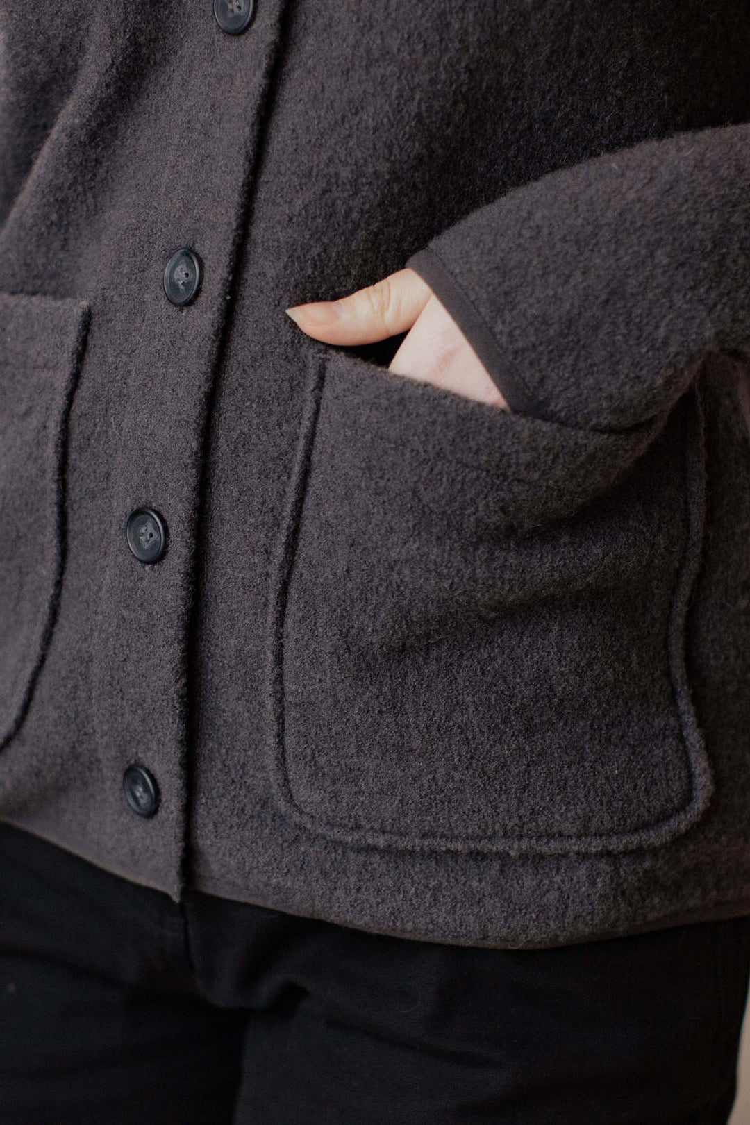 A person wears the Bridge & Burn Whit Cardigan in Charcoal, one hand partly in a large patch pocket. The close-up highlights the jacket's boiled wool texture and details around the torso and hip area.