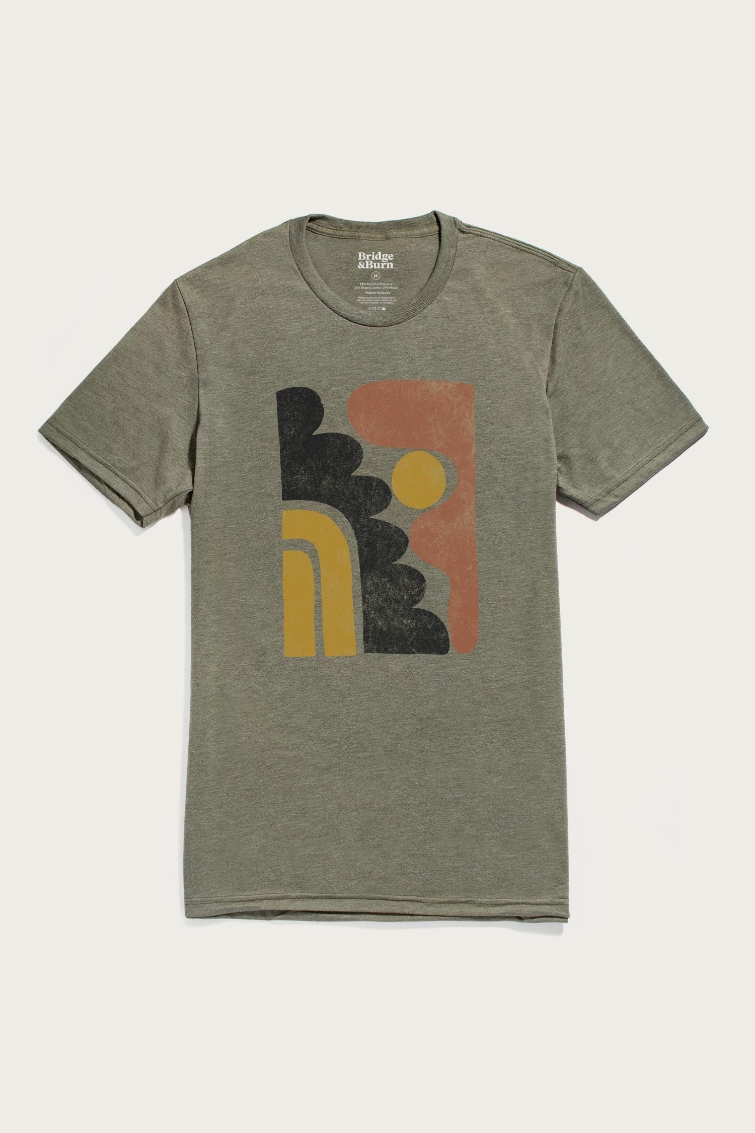 The Men's Ladera Tee by Bridge & Burn in olive features a lightweight design and a centered abstract graphic with black, mustard yellow, and rust shapes resembling a stylized sun and arches.