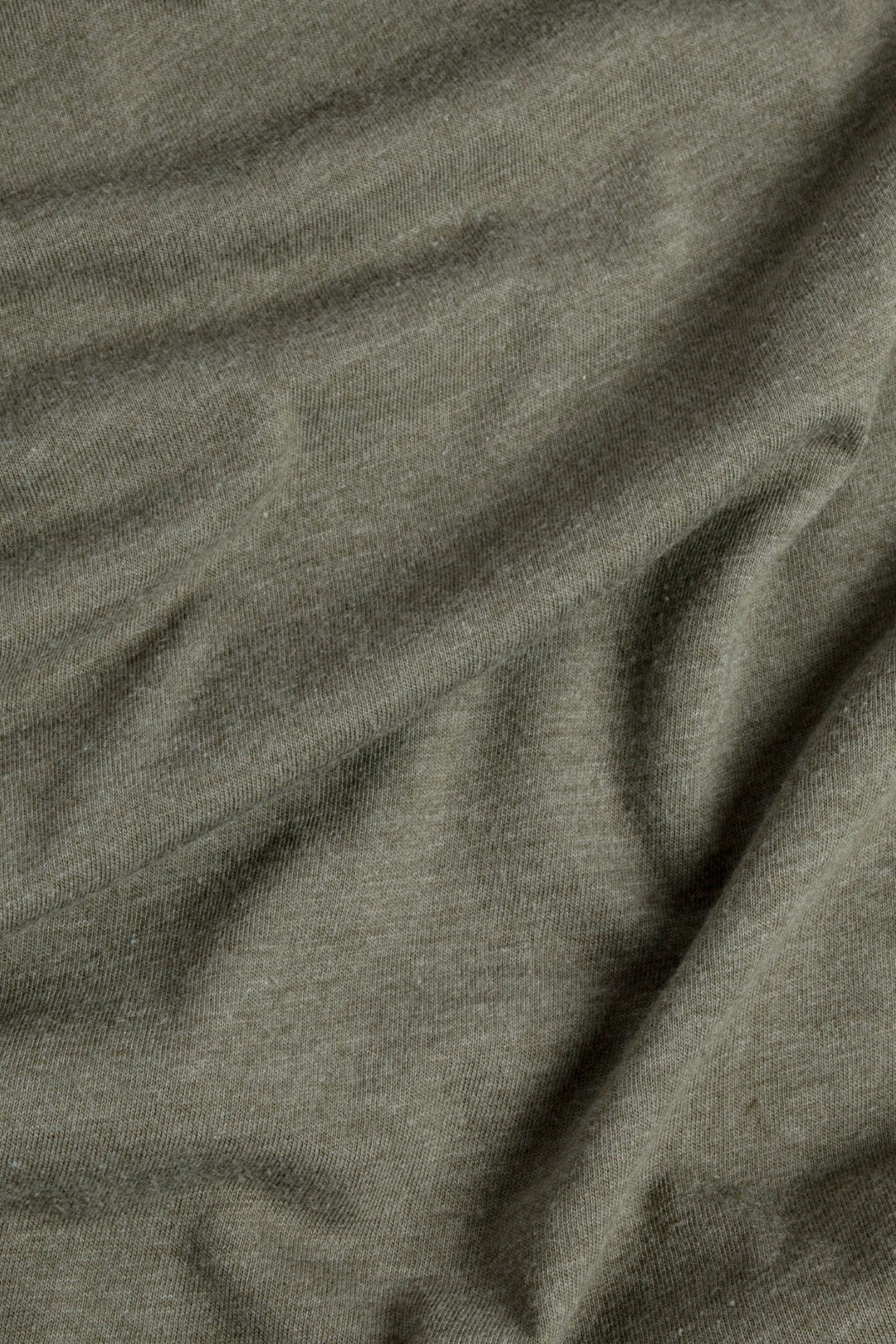 A close-up of the Bridge & Burn Men's Ladera Tee in Olive highlights its soft, lightweight fabric with visible knit texture and gentle folds that create subtle shadows.