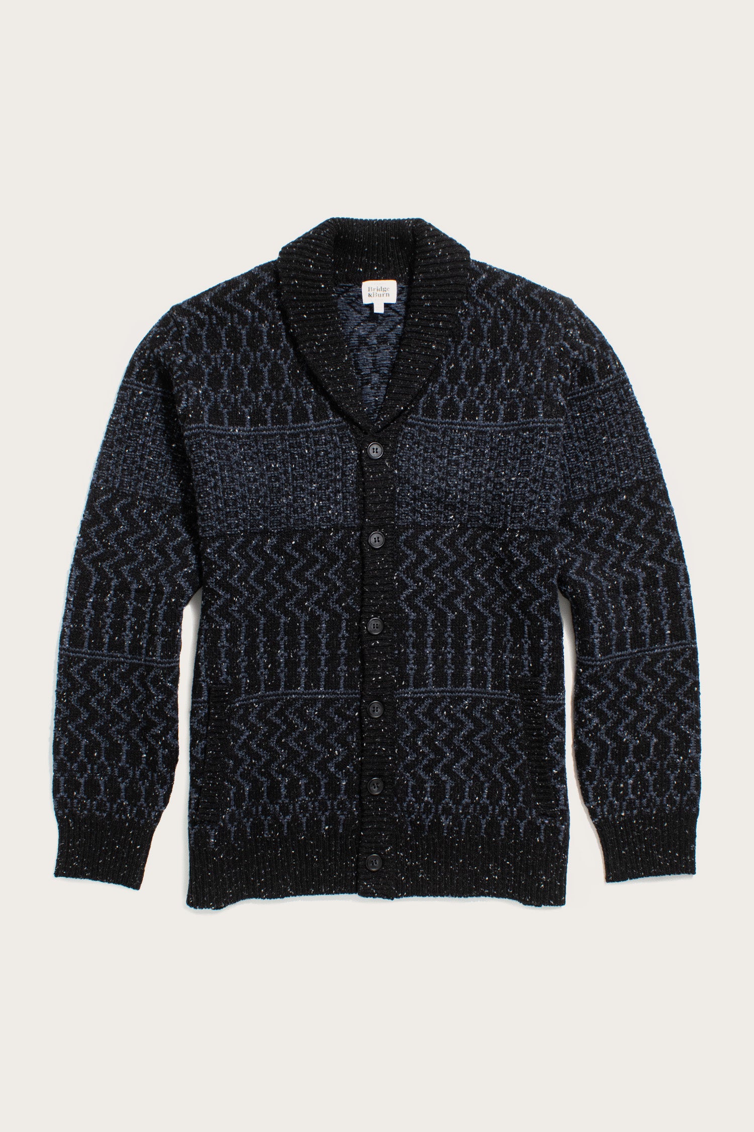 The Bridge & Burn Anders Cardigan in Midnight Tweed features a dark blue and black geometric pattern, cozy shawl collar, button front, and long sleeves. Crafted from RWS certified wool for comfort and sustainability.