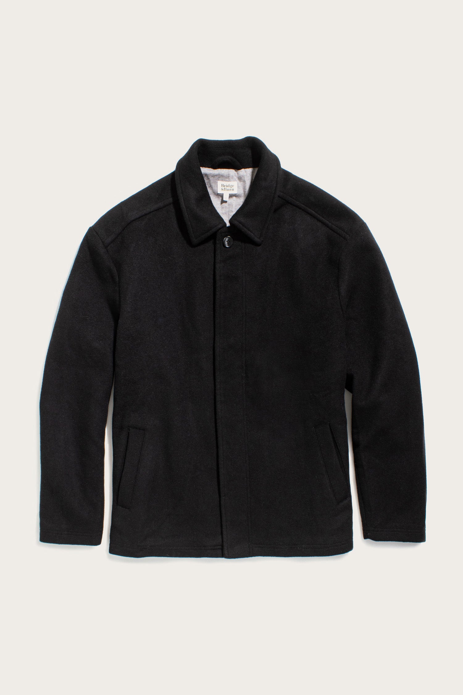 The Bridge & Burn Clive Car Coat in black features a collar, long sleeves, two slanted front pockets, and a concealed front closure for cold-weather comfort, shown laid flat on a light background.