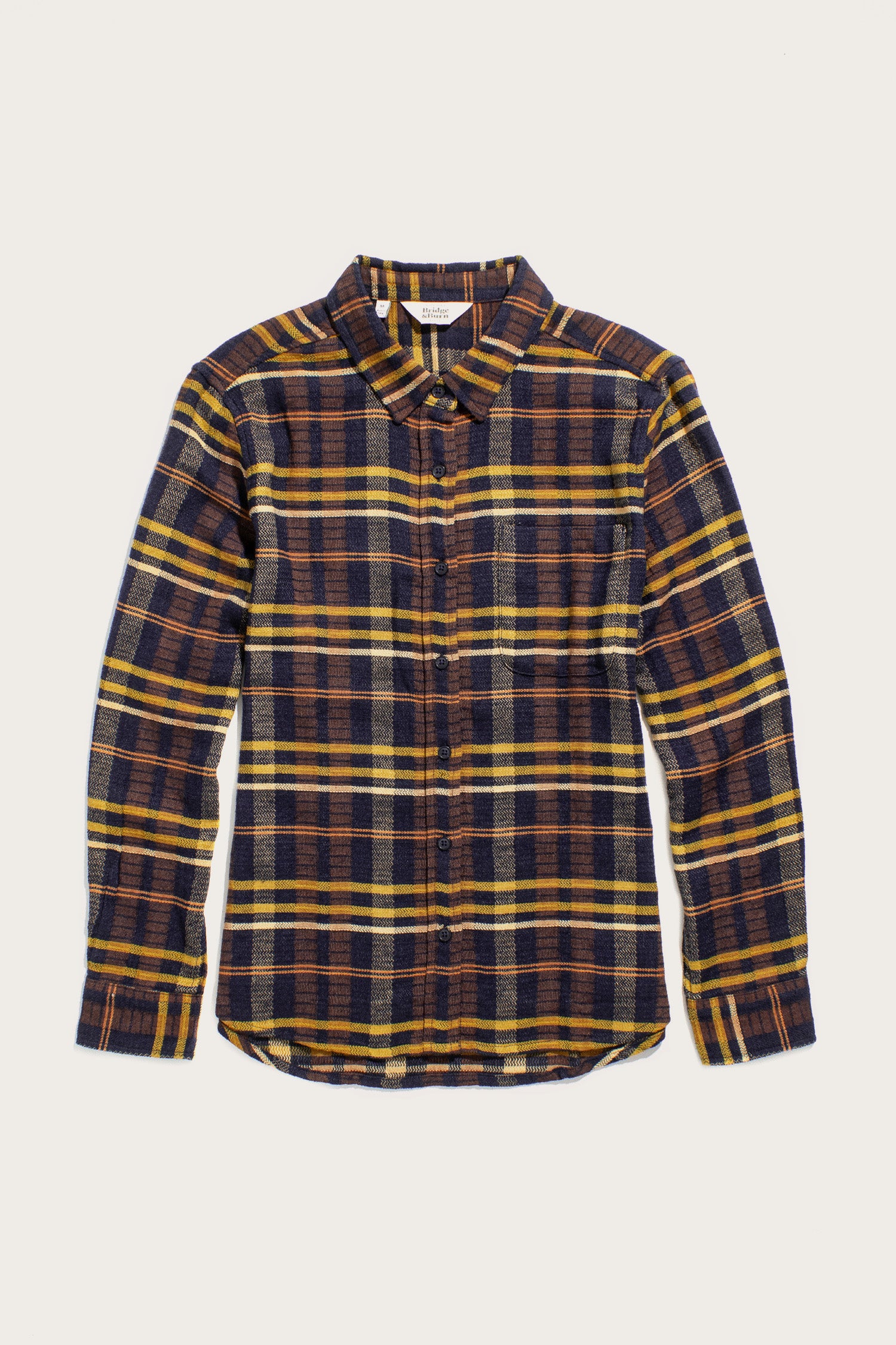 The Bridge & Burn Ash Slim Shirt in Desert Dawn Plaid is a slim fit, long sleeve button-up made from organic cotton, featuring navy blue, yellow, and brown tones. Shown flat on a white background.
