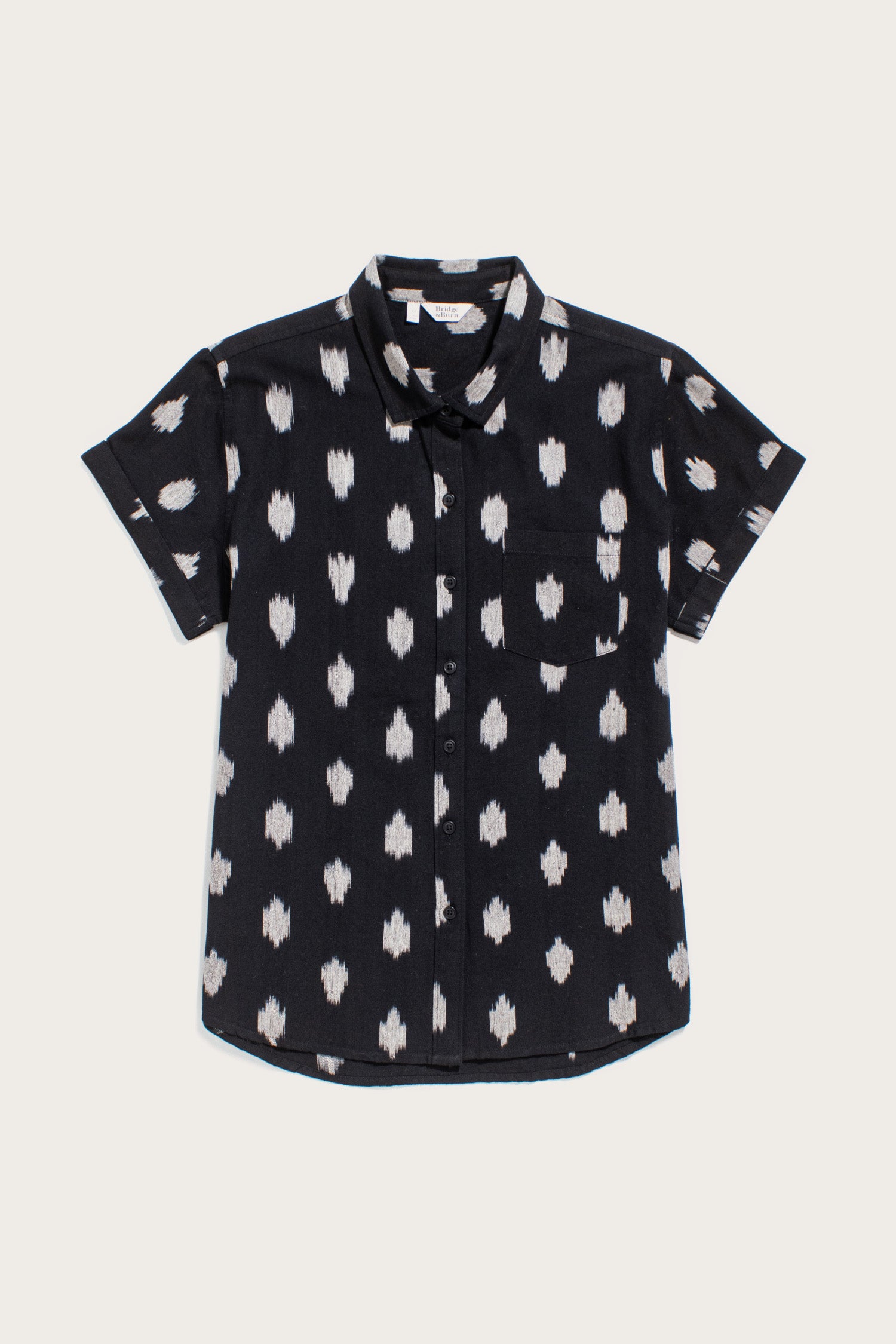 The Bridge & Burn Bea Shirt in Eclipse Ikat features a black background with a white abstract dot pattern, short sleeves, a left chest pocket, and is crafted from 100% cotton. The shirt is shown laid flat on a plain light background.
