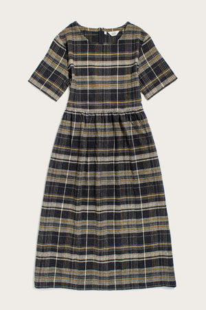 The Perry Dress in Volcanic Plaid by Bridge & Burn is a midi dress with short sleeves, made from recycled cotton. It features a dark navy, yellow, and white plaid pattern with a fitted bodice and gathered skirt.