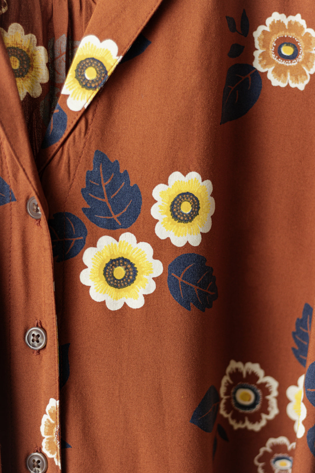 The Bridge & Burn Mila Cropped Shirt in Rose Floral features brown modal fabric with yellow and white flower prints, dark blue leaves, and brown buttons. This breathable shirt offers all-day comfort.