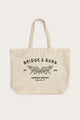 The Fox Tote / Natural by Bridge & Burn is a beige cotton canvas tote with two handles, featuring BRIDGE & BURN and twin foxes artwork. It says 