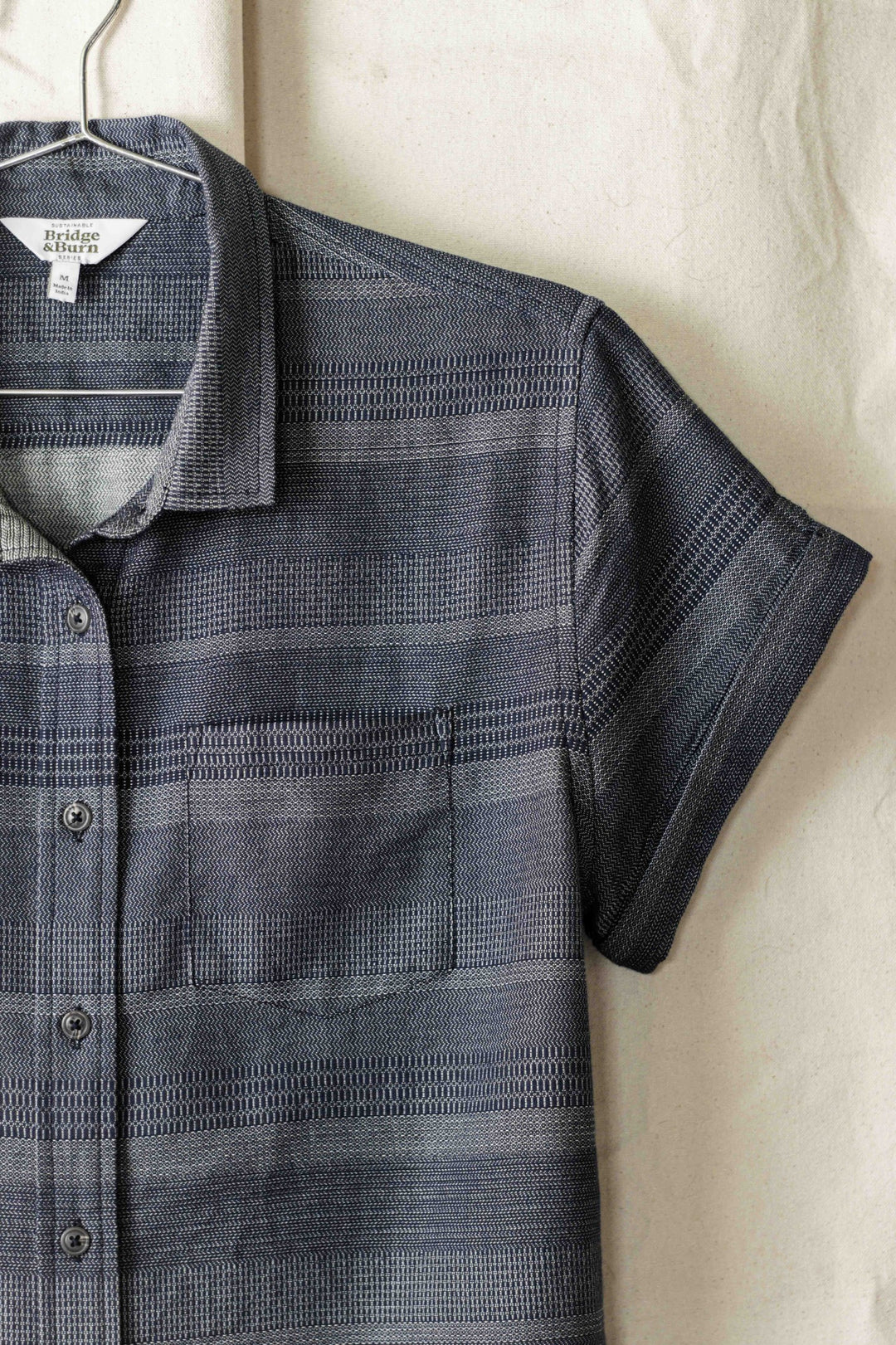 The Bea Shirt / Cascade Weave by Bridge & Burn, a tailored-fit short-sleeve button down with gray and navy horizontal stripes, features a collar, chest pocket, and is made from soft organic cotton for comfort.