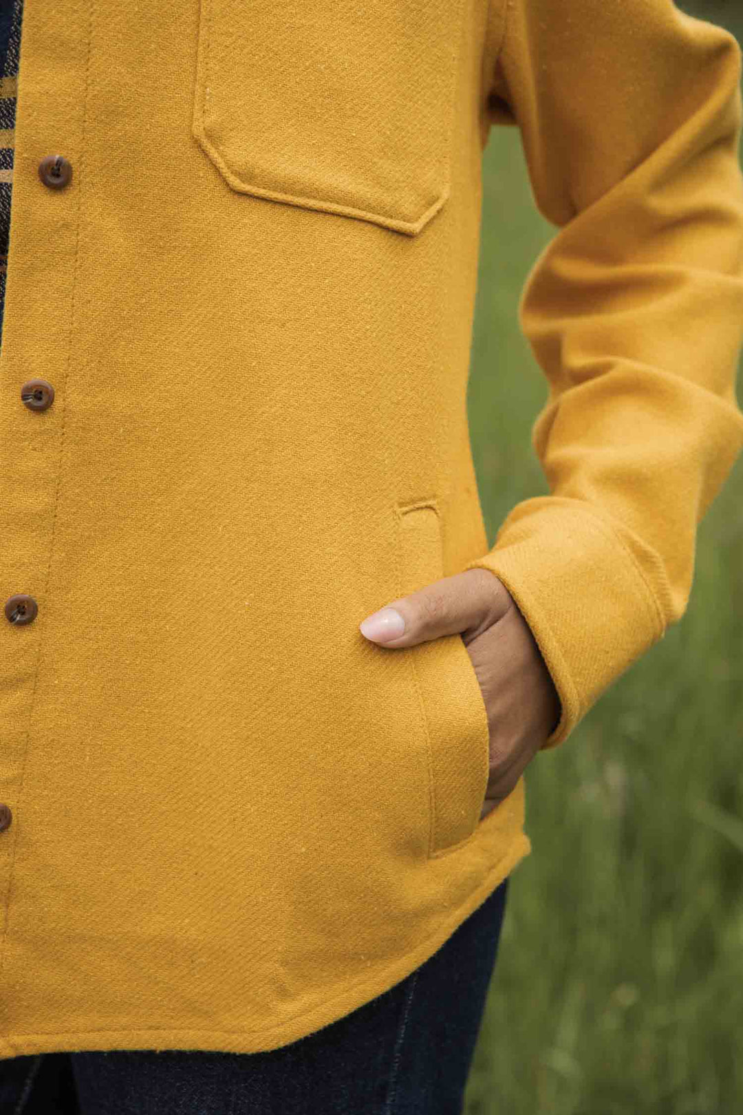 A person wears the Bridge & Burn Dawson Overshirt in Antique Gold, made from recycled cotton. Pictured outdoors with one hand in the pocket, only the torso, arm, and hand are visible, highlighting a sustainable clothing choice.
