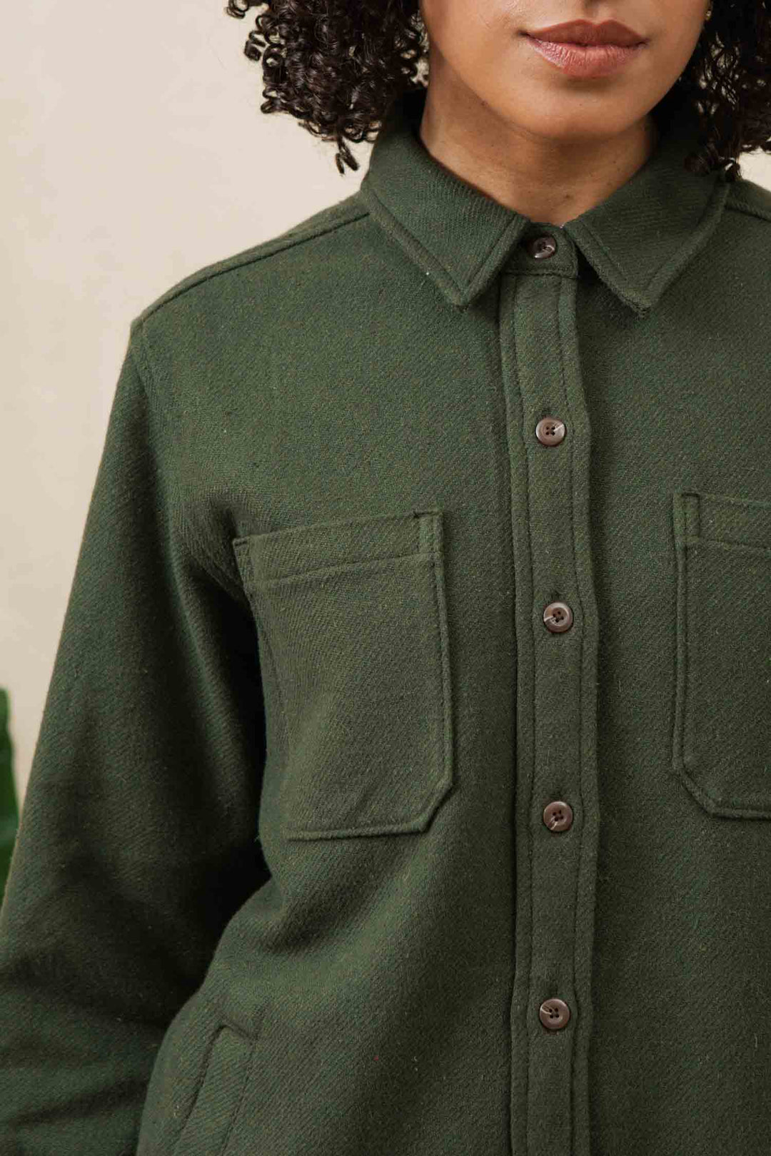A person wearing the Bridge & Burn Dawson Overshirt in Dark Sage with two chest pockets is shown from shoulders to mid-torso, with curly hair and lower face partially visible.