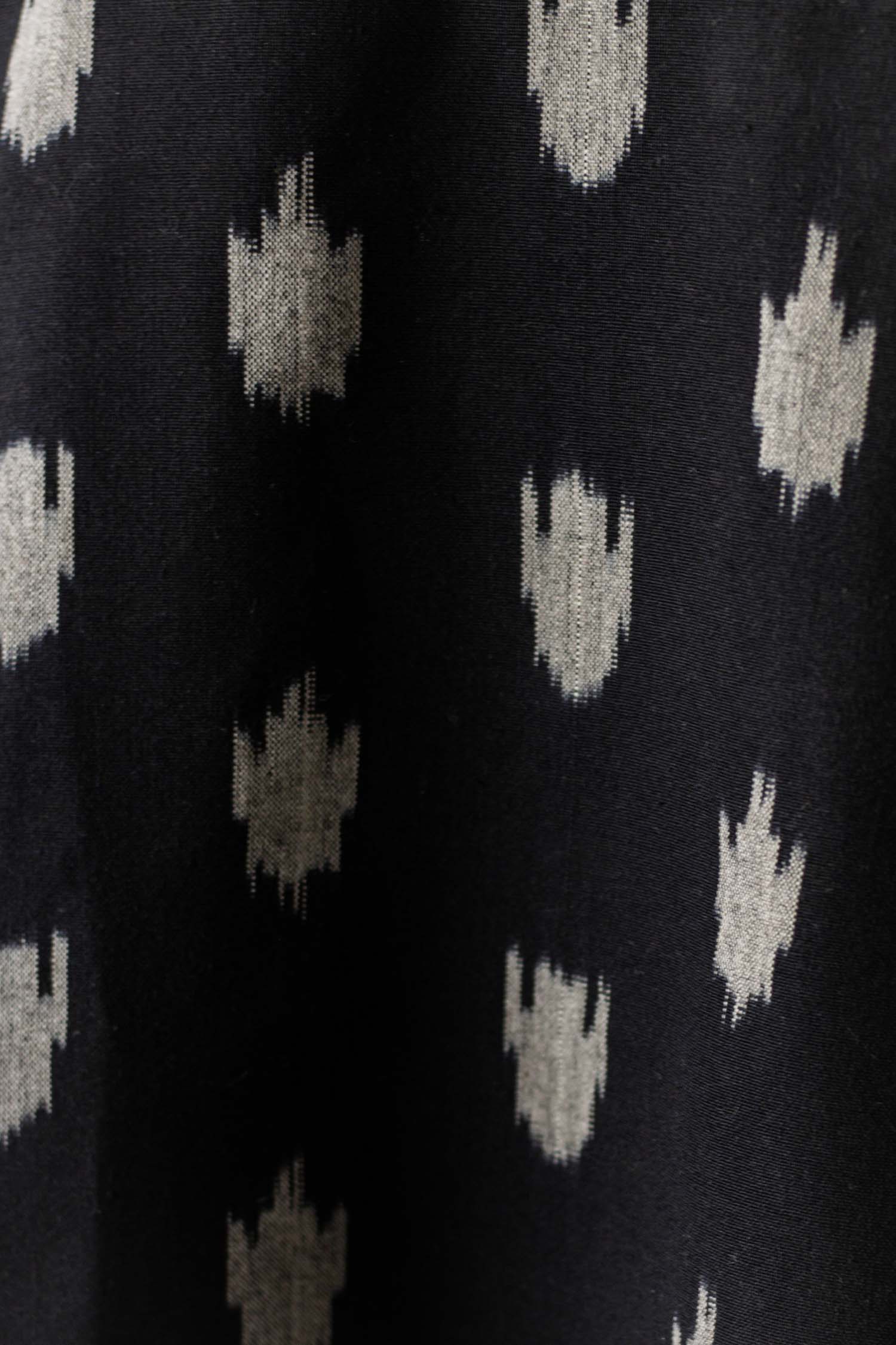 Close-up of the Delia Shirt Dress in Eclipse Ikat by Bridge & Burn, featuring black organic cotton fabric with a repeating pattern of small, irregular white abstract geometric motifs.