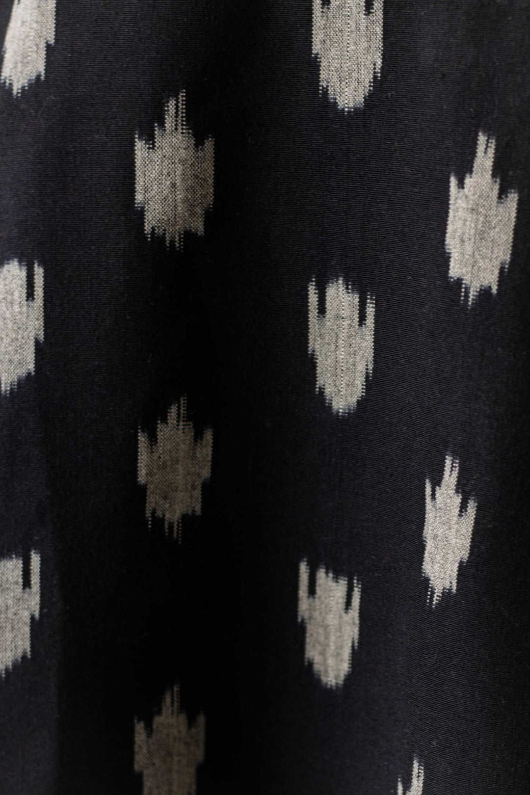 Close-up of the Delia Shirt Dress in Eclipse Ikat by Bridge & Burn, featuring black organic cotton fabric with a repeating pattern of small, irregular white abstract geometric motifs.