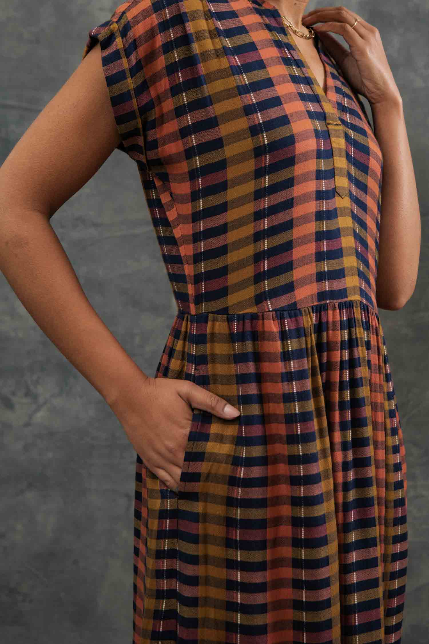 The Ira Dress by Bridge & Burn features knee-length, short dolman sleeves, a v-neck, Alpenglow Stripe pattern in mustard yellow, rust orange, navy blue, and black. Made from eco-friendly viscose with a gathered waist and relaxed fit.