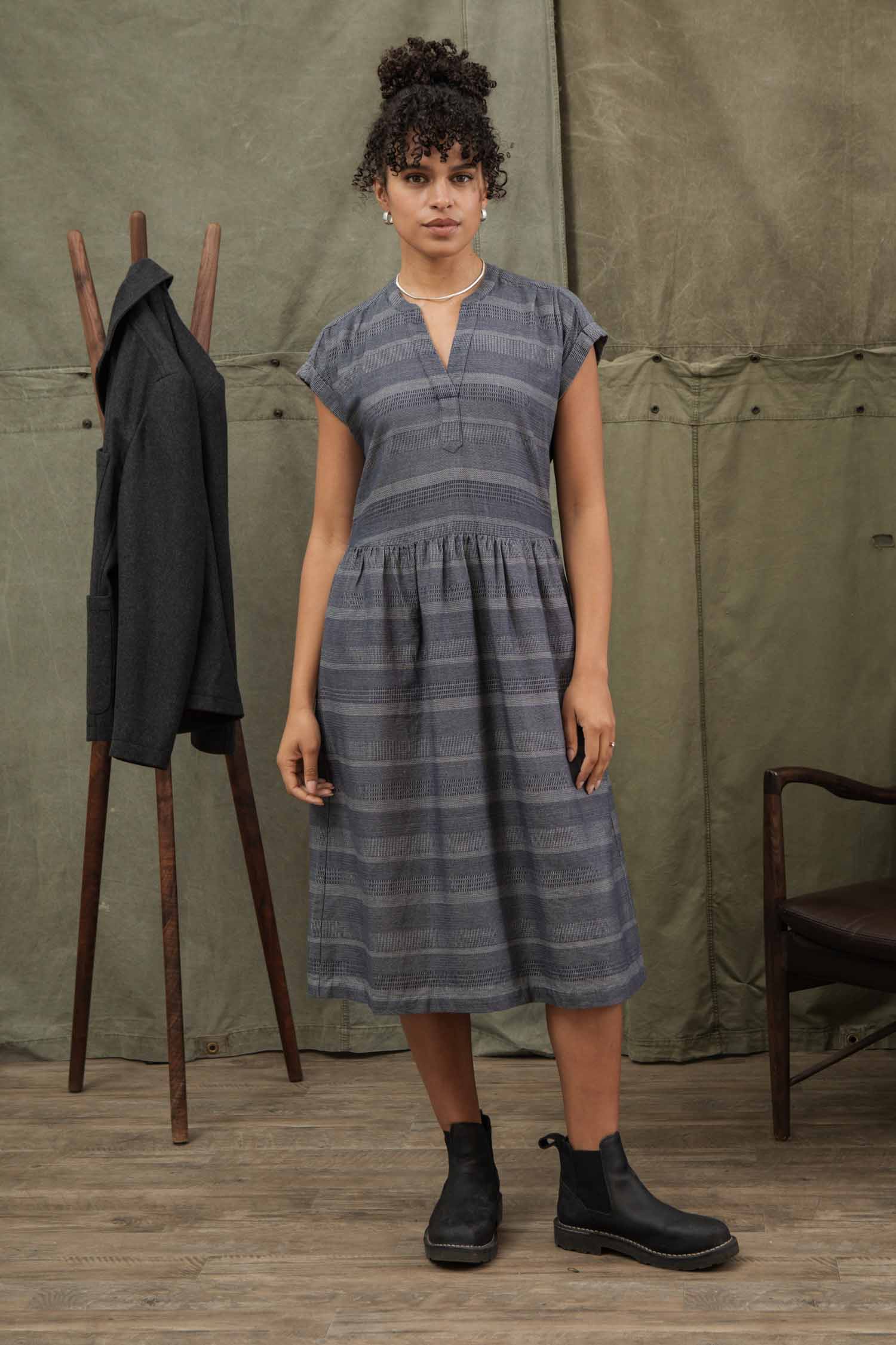 The Bridge & Burn Ira Dress in Cascade Weave is a short-sleeve, knee-length organic cotton dress with subtle gray stripes, V-neckline, gathered waist, and a relaxed pullover fit for effortless comfort.