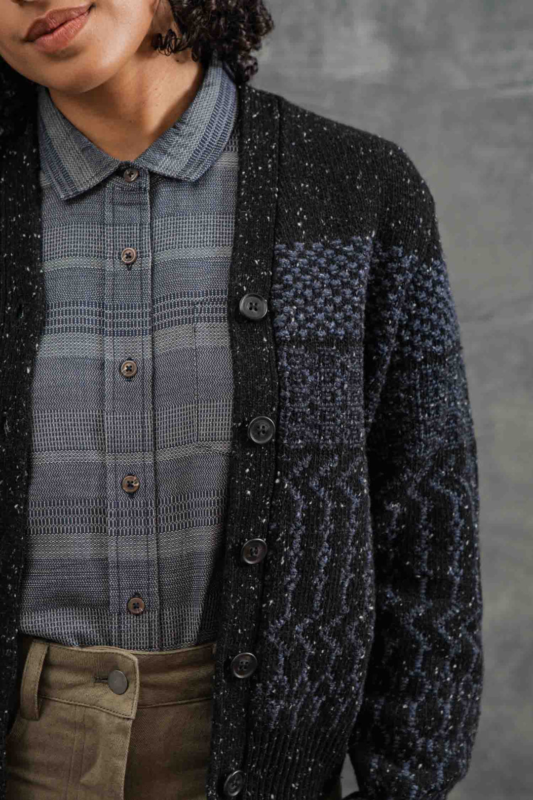 A person wears the Bridge & Burn Juneau Cardigan in Midnight Tweed over a gray plaid button-up shirt, with only their lower face and upper torso visible against a plain gray background.