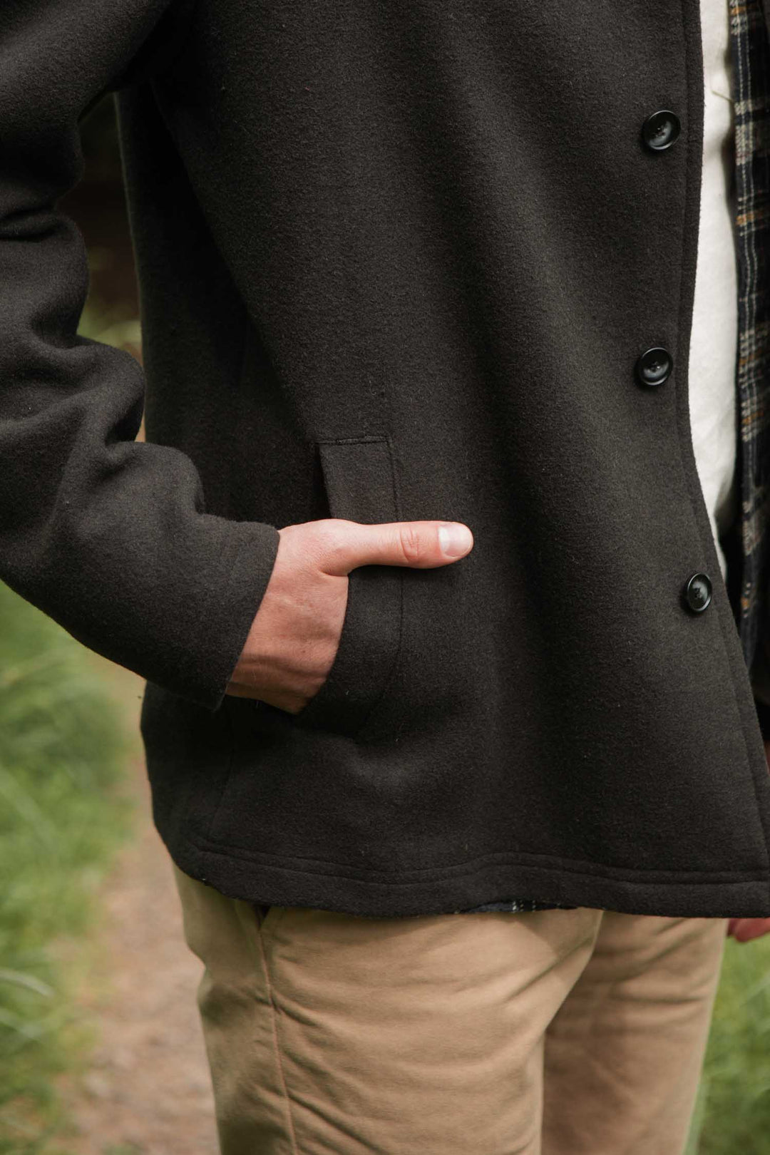 A person wears the Bridge & Burn Clive Car Coat in Deep Sage, with a hand in their pocket. Only their torso and part of an arm and hand are visible, suggesting comfortable cold-weather style. Tan pants complete the outdoor look.