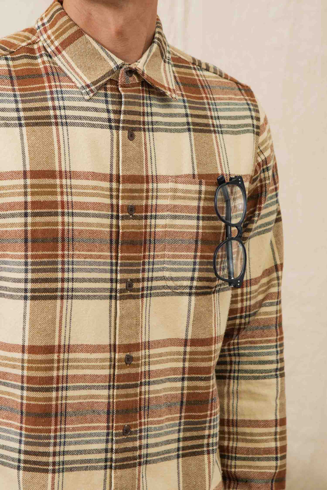 A person wearing the Bridge & Burn Larson Shirt in Latte Plaid with glasses tucked into the chest pocket. Only their upper torso is visible.