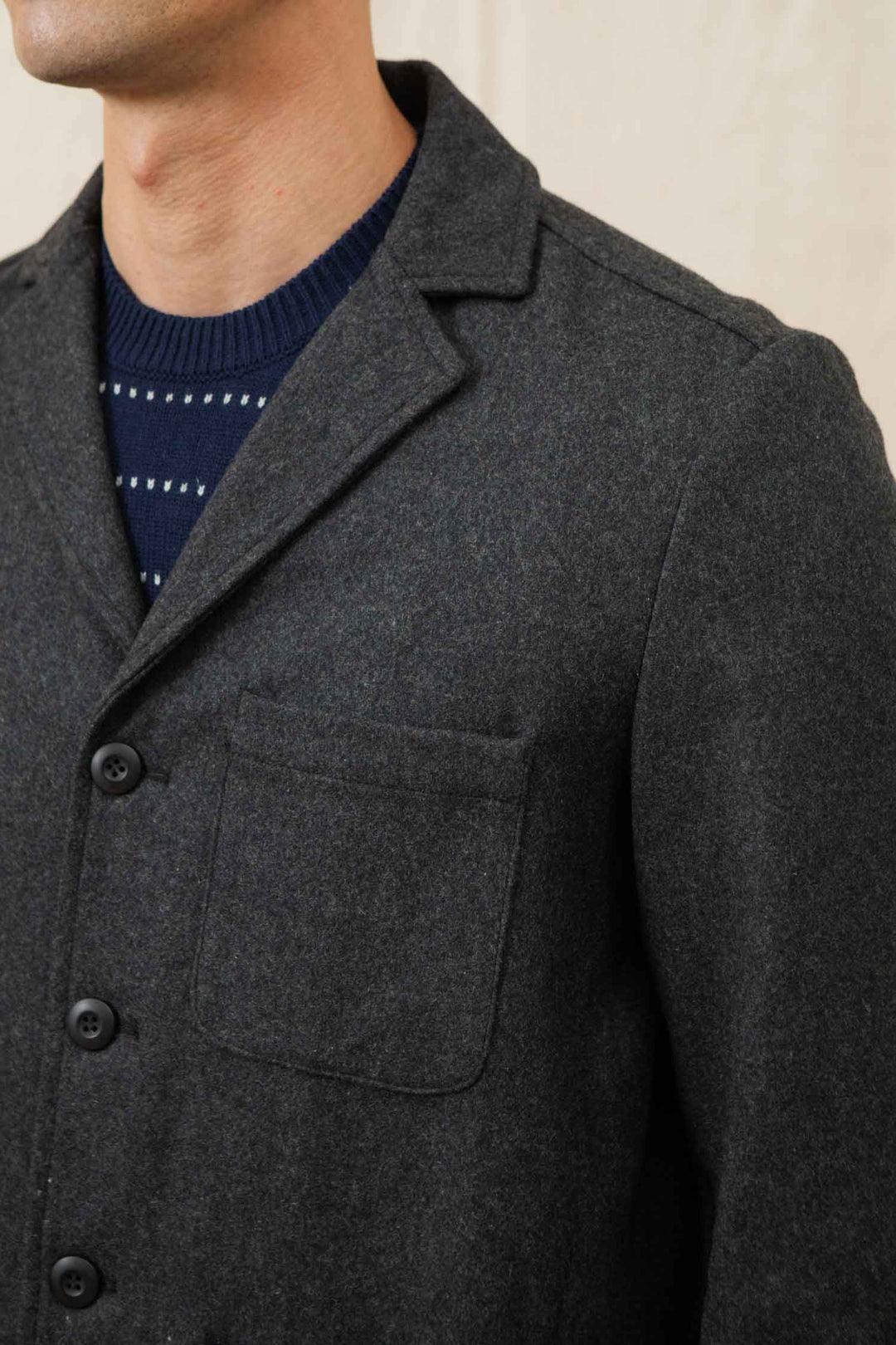 A close-up of a person wearing the Bridge & Burn Nate Chore Blazer in Onyx Wool over a navy sweater with white dots. The winter-ready blazer features a chest pocket and black buttons; the person's face is not shown.
