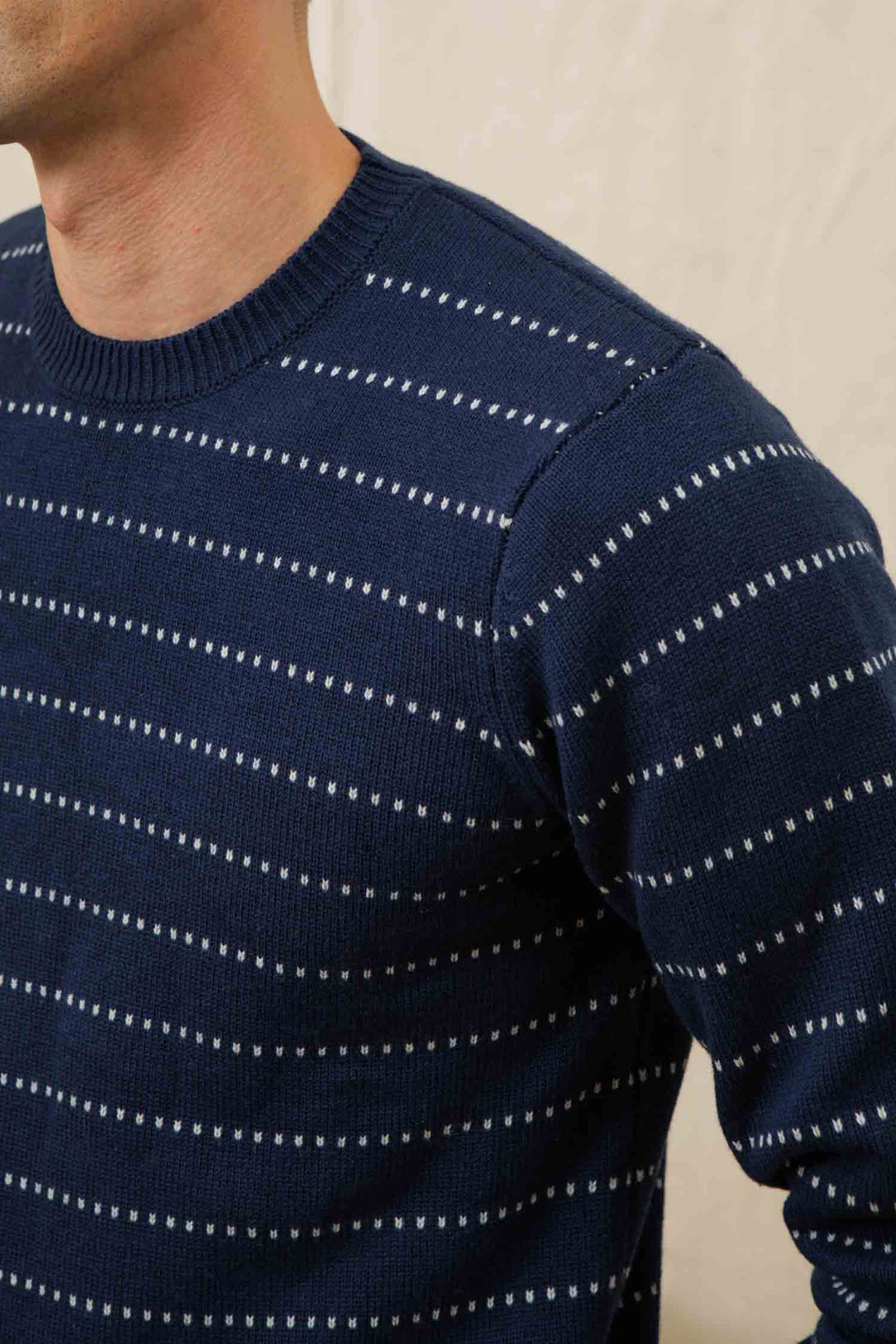 A person wears the Bridge & Burn Orson Sweater in Navy Dotted Path, featuring small white horizontal dotted stripes; only their upper torso and part of their face are visible against a light background.