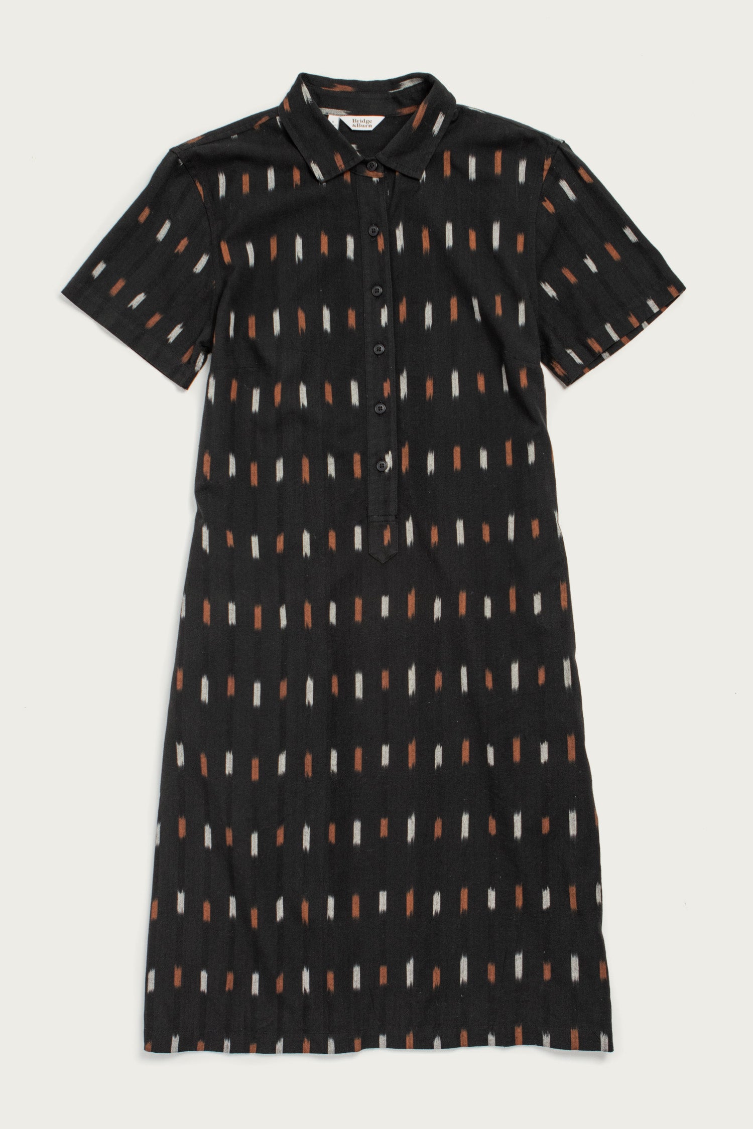 The Delia Dress by Bridge & Burn in Dotted Horizon is a short-sleeved, knee-length black organic cotton shirt dress with a collar, buttoned front, and vertical orange, white, and beige rectangle pattern.