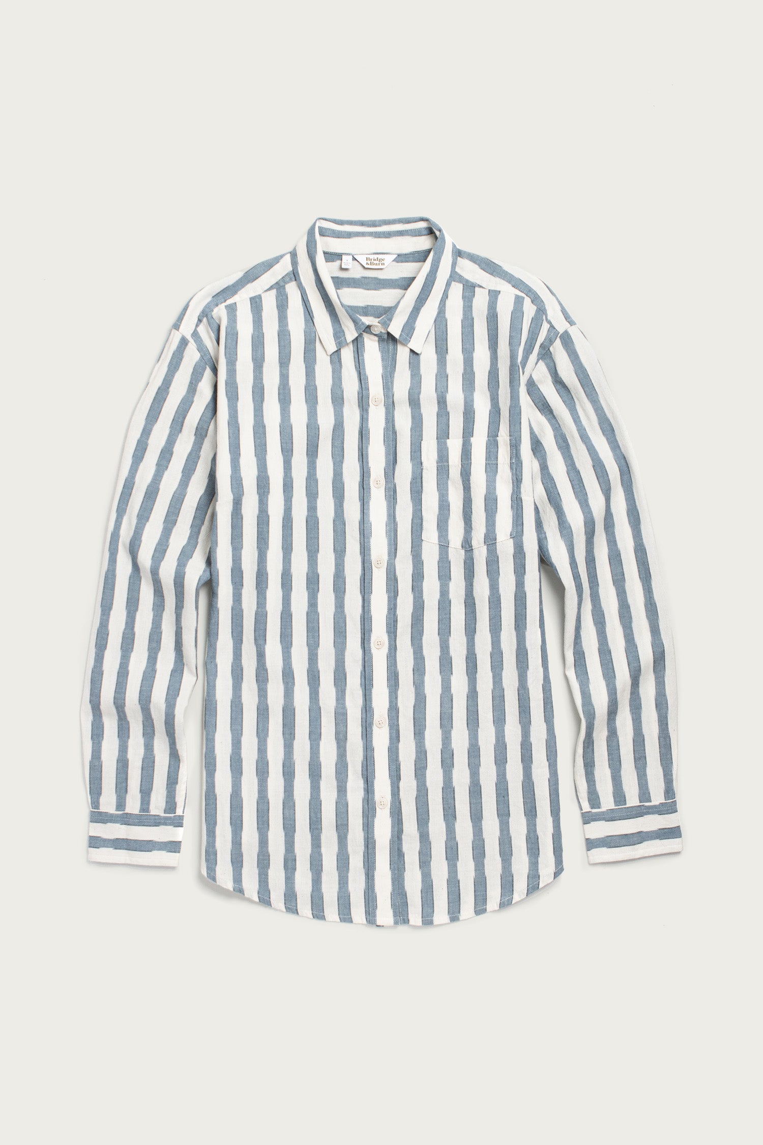 The Haley Shirt / Beach Stripe by Bridge & Burn features vertical blue and white stripes, a relaxed fit, classic collar, chest pocket, and long sleeves—an essential laid flat on a white background.
