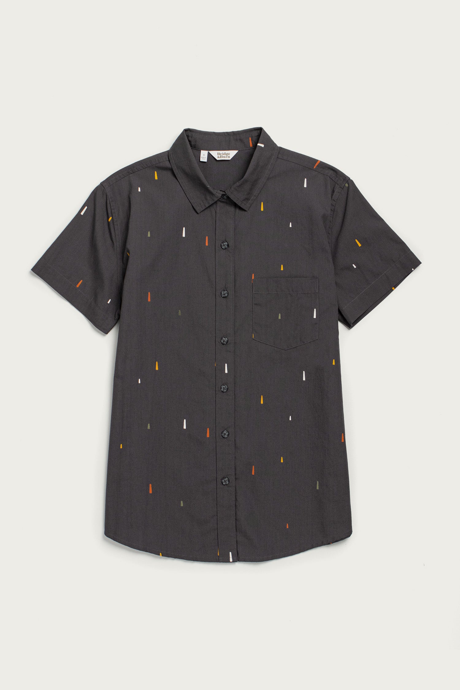The Bridge & Burn Lana Shirt in Midnight Rain is a relaxed fit, short sleeve black button-up with a collar and chest pocket, made from 100% cotton and detailed with small red, yellow, and white vertical lines. Laid flat on white.