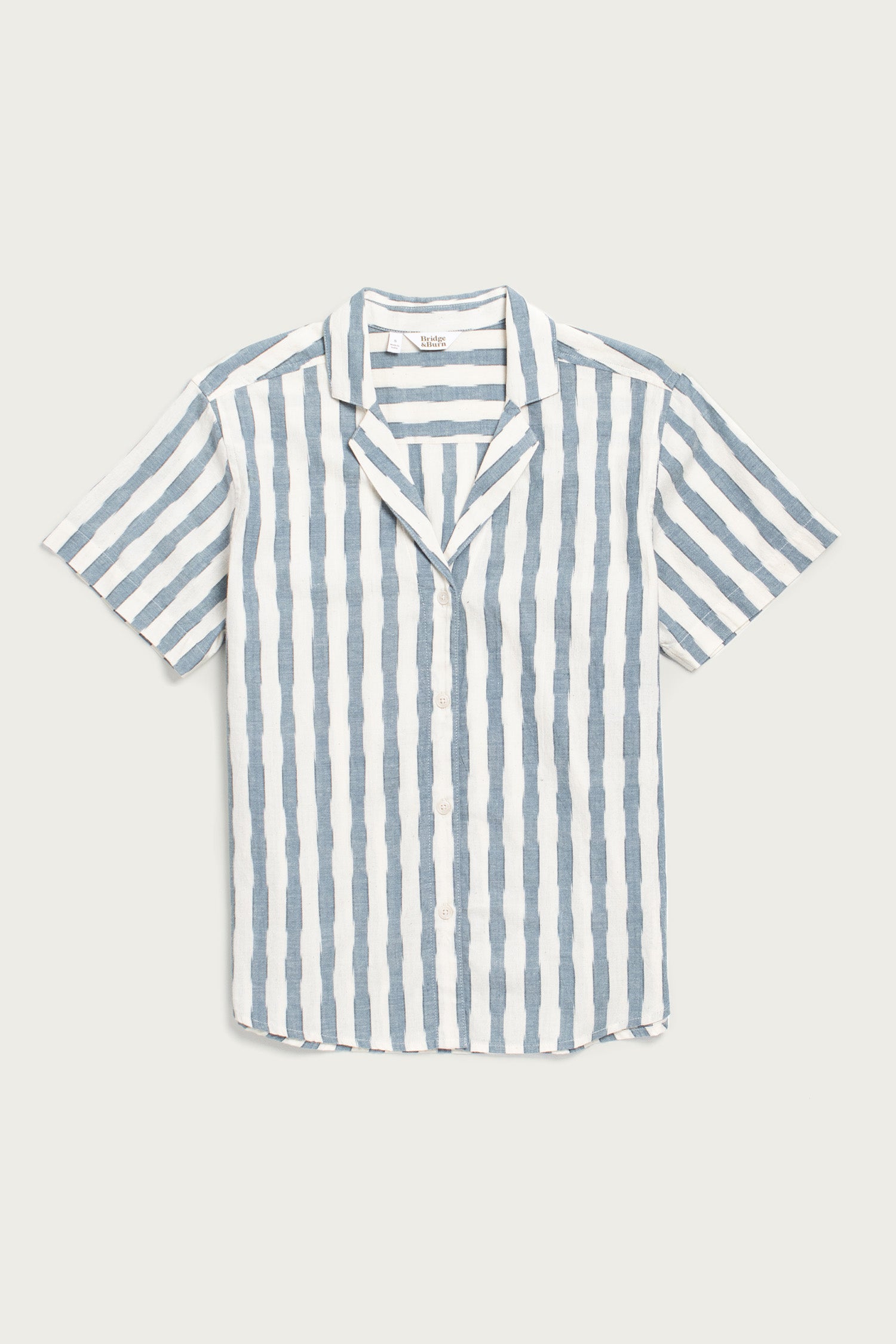 The Wren Shirt / Beach Stripe by Bridge & Burn is a relaxed-fit, short-sleeve cotton shirt with blue and white stripes, notched collar, and retro style—shown laid flat on a plain background.
