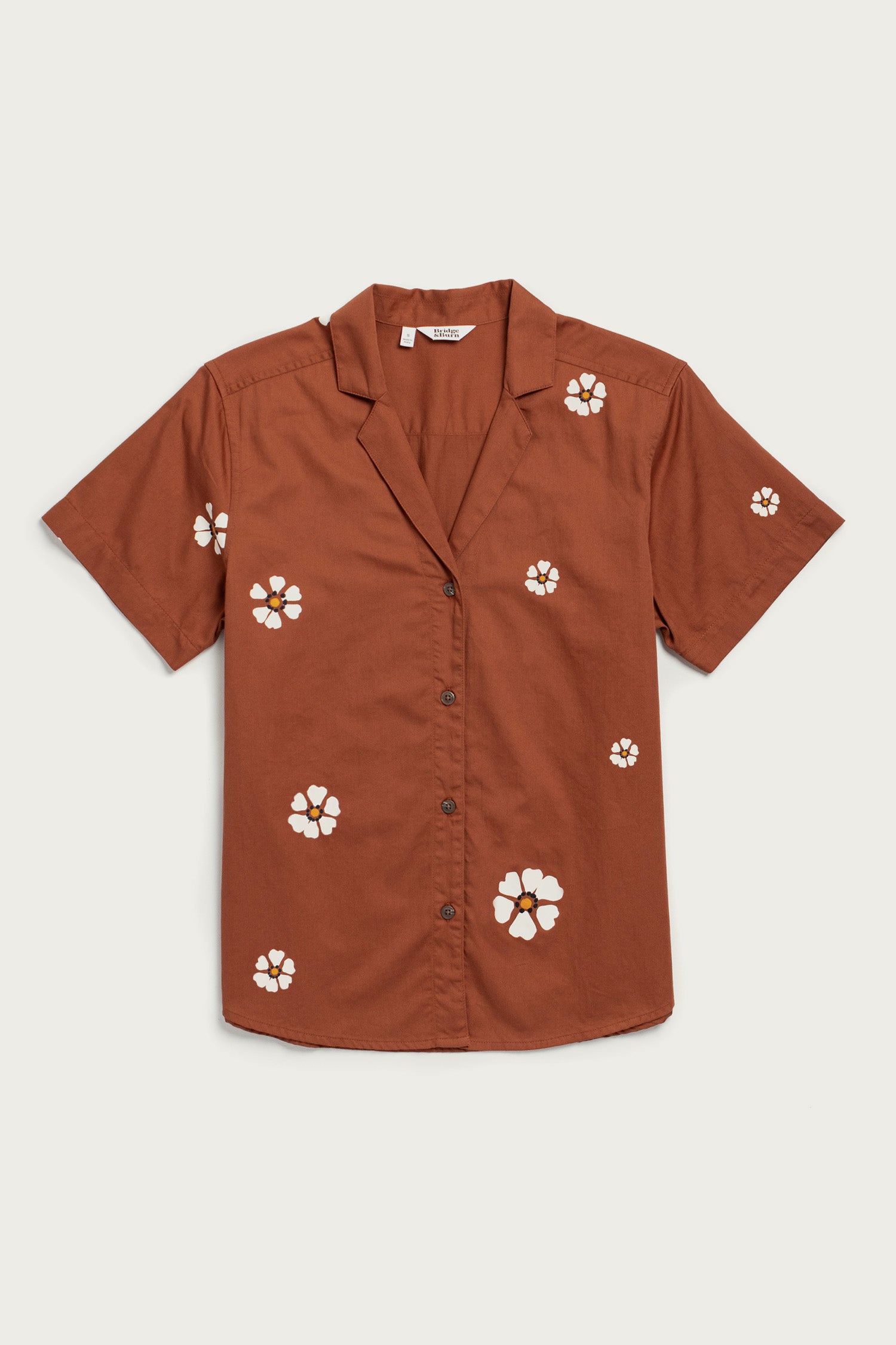 The Wren Shirt by Bridge & Burn in Redstone Bloom is a breathable cotton, short-sleeved button-up with a notched collar and scattered white and yellow floral prints for a relaxed fit.