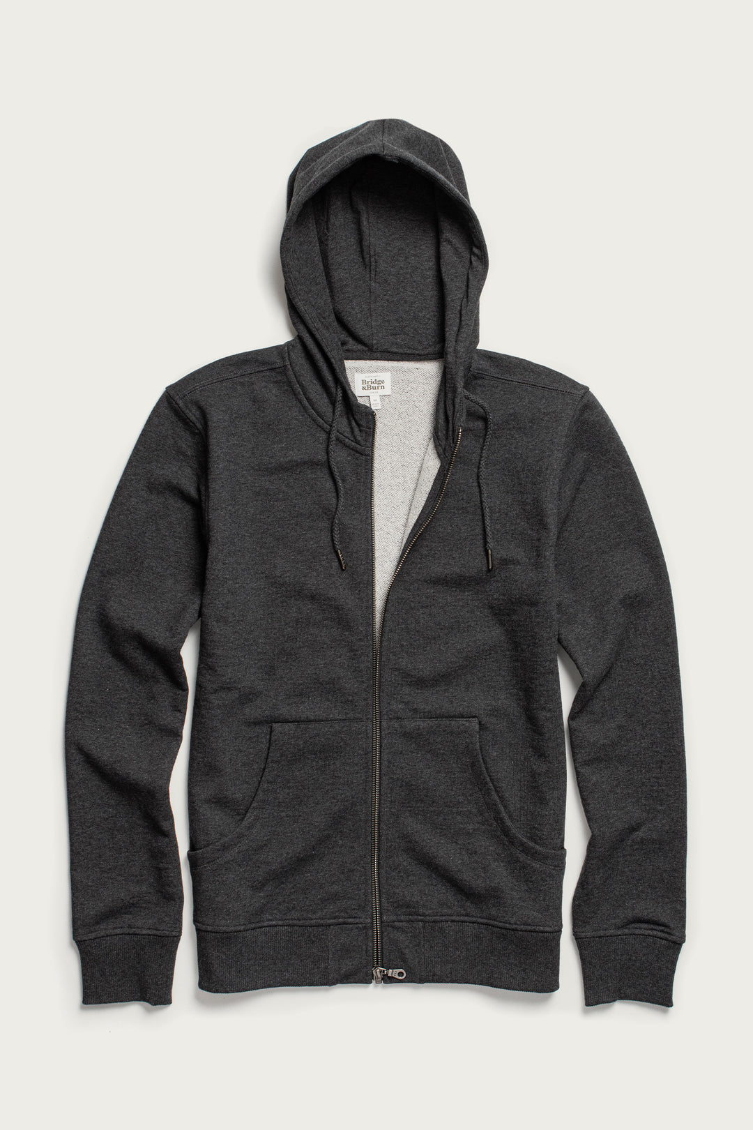 The Ridge Hoodie in Graphite by Bridge & Burn is a zip-up hoodie made from soft organic cotton, featuring a classic hood for comfort.