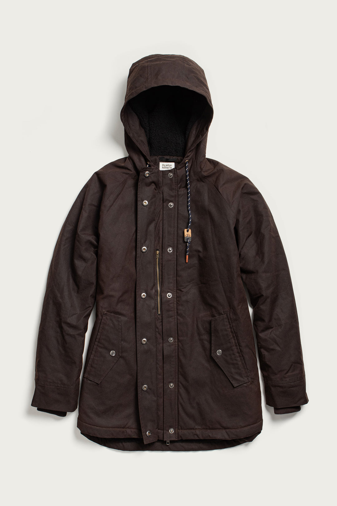 The Bridge & Burn Sequoia Parka in umber waxed canvas features a hood with drawstring, snap buttons, front zipper, two large flap pockets, and fleece lining, shown laid flat on a light background.