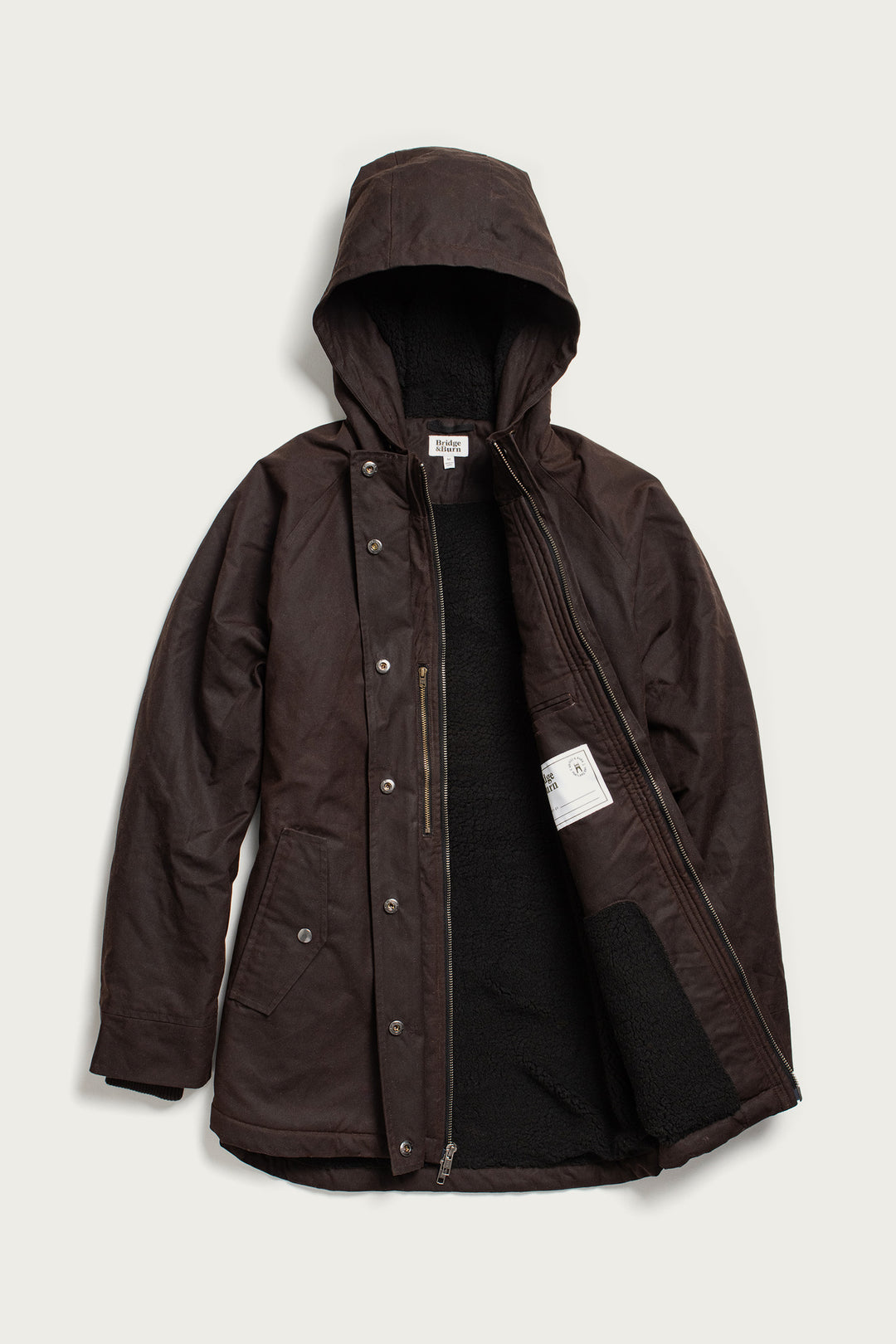 The Bridge & Burn Sequoia Parka in umber waxed canvas features a dark brown hood, zip and snap closures, cozy black fleece lining with an interior pocket and white label, two front flap pockets, and a relaxed fit.